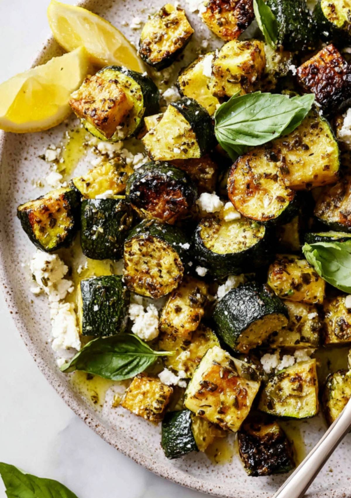 Sliced, oven-roasted zucchini tossed with feta cheese and fresh basil on a ceramic plate.