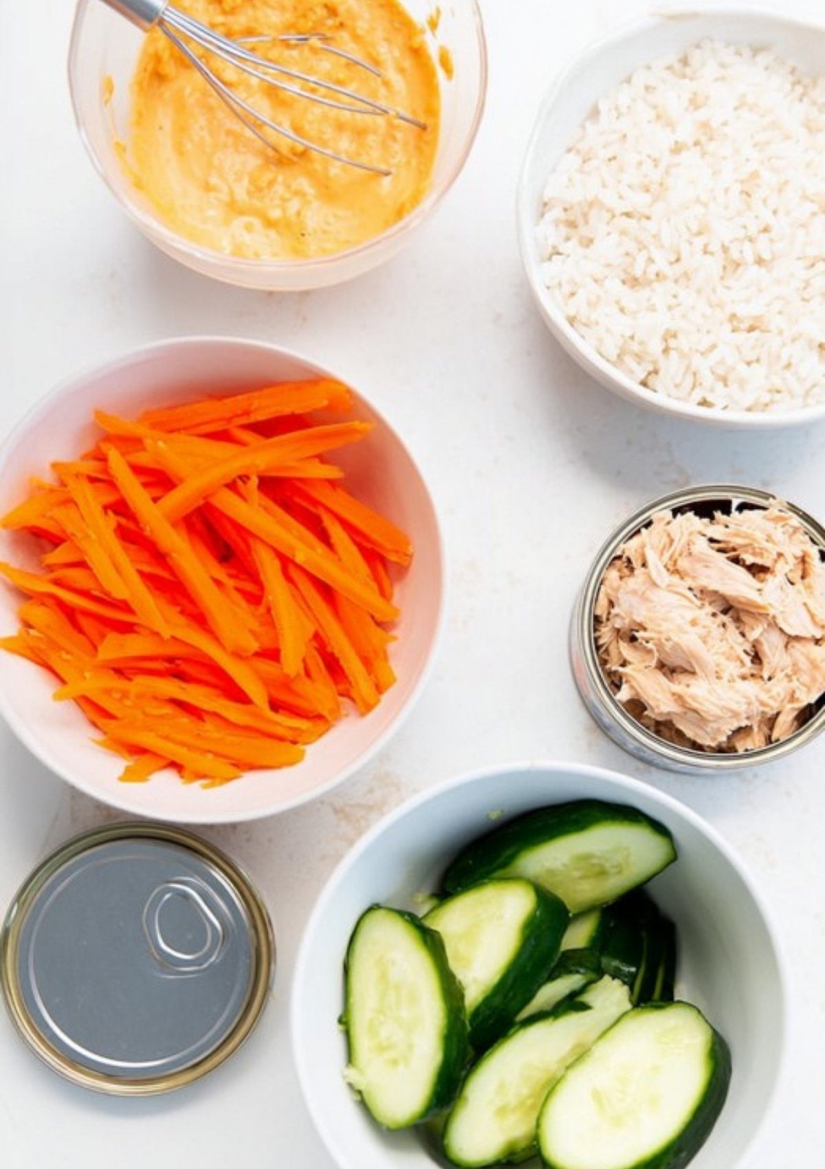 Bowls of rice, tuna, carrots, cucumber, and spicy mayo sauce for assembling spicy tuna rice bowls.