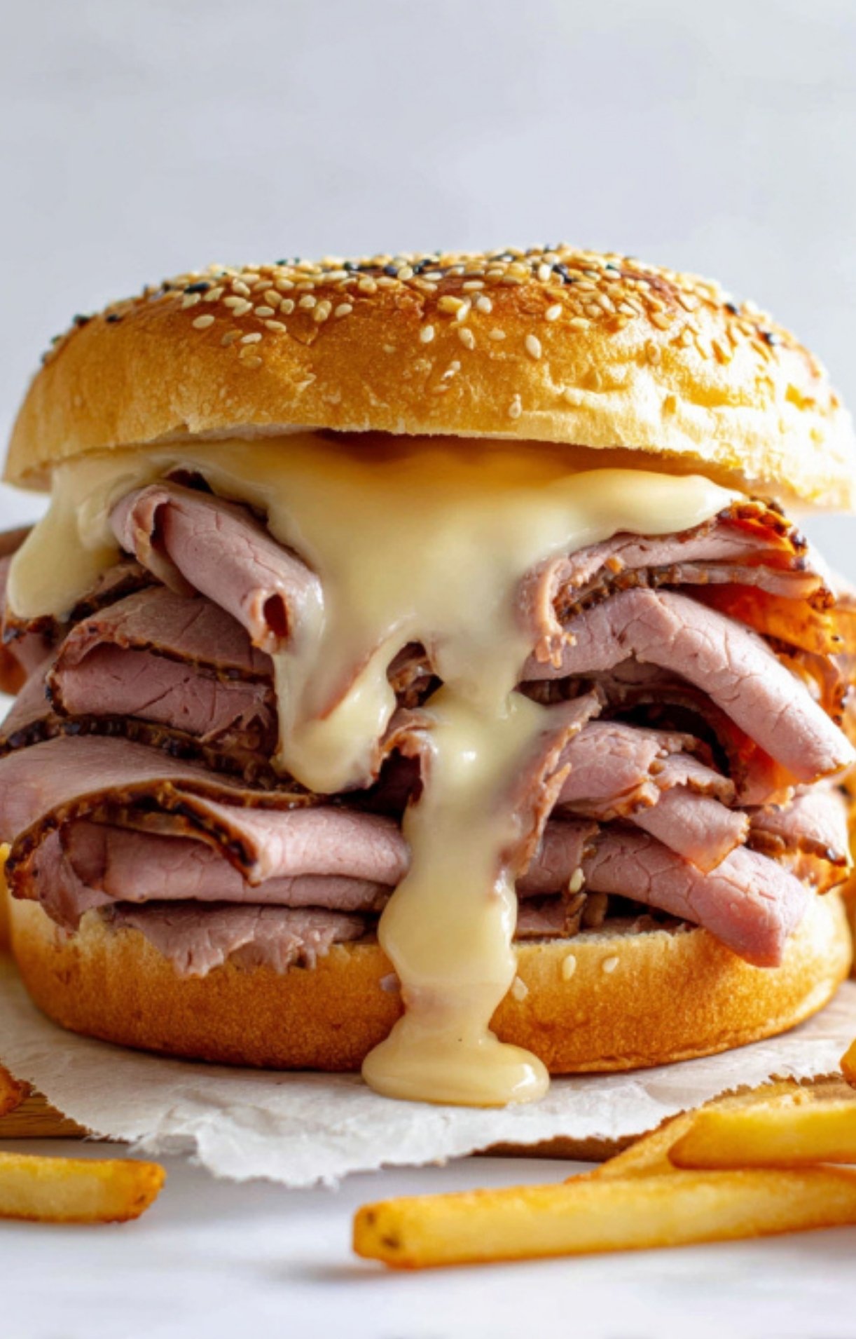 Sesame seed bun stacked with sliced roast beef and drizzled with creamy cheddar cheese sauce, served with crispy fries