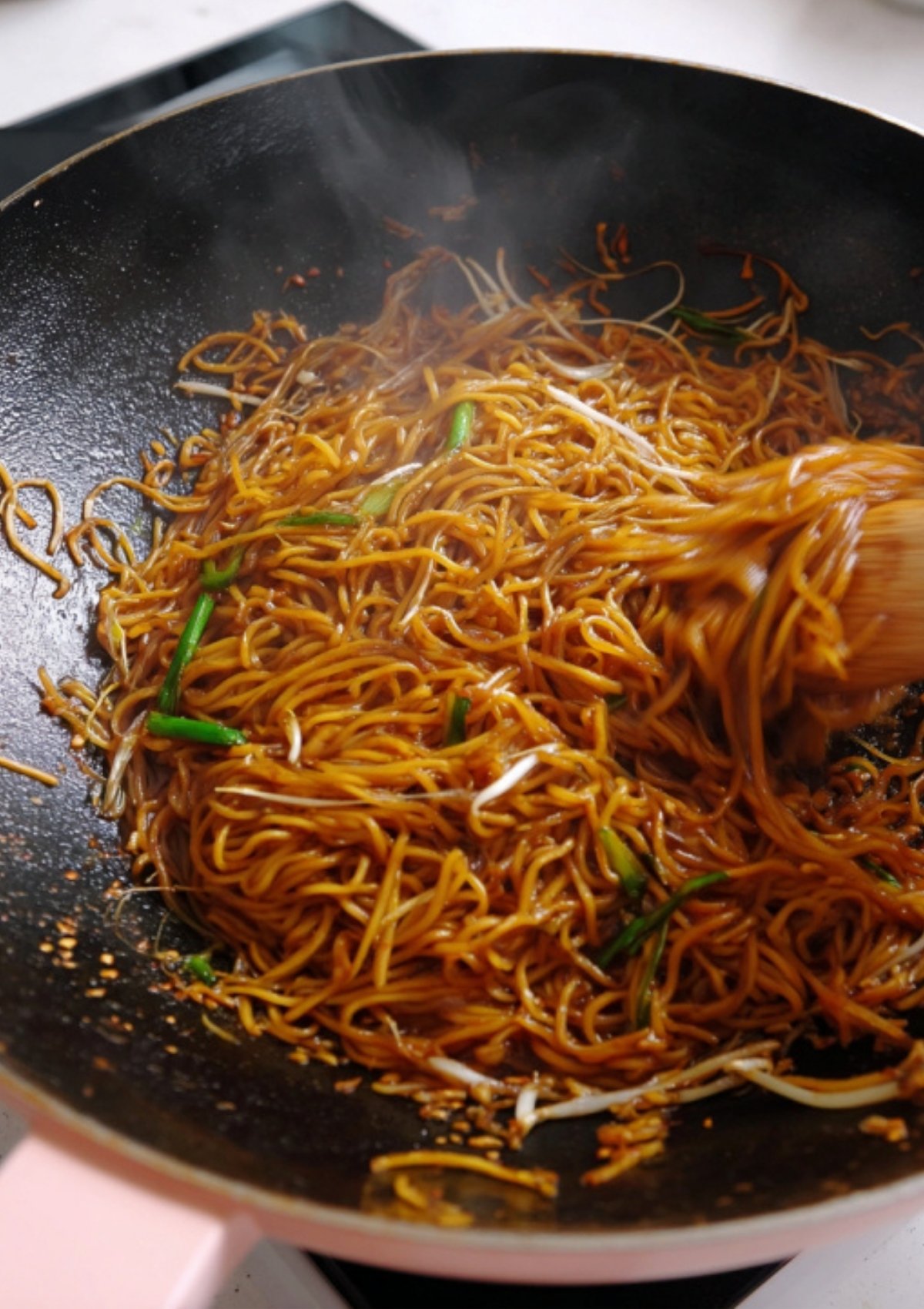 Soy sauce noodles being stir-fried with crunchy bean sprouts and green onions for an easy 10-minute meal.