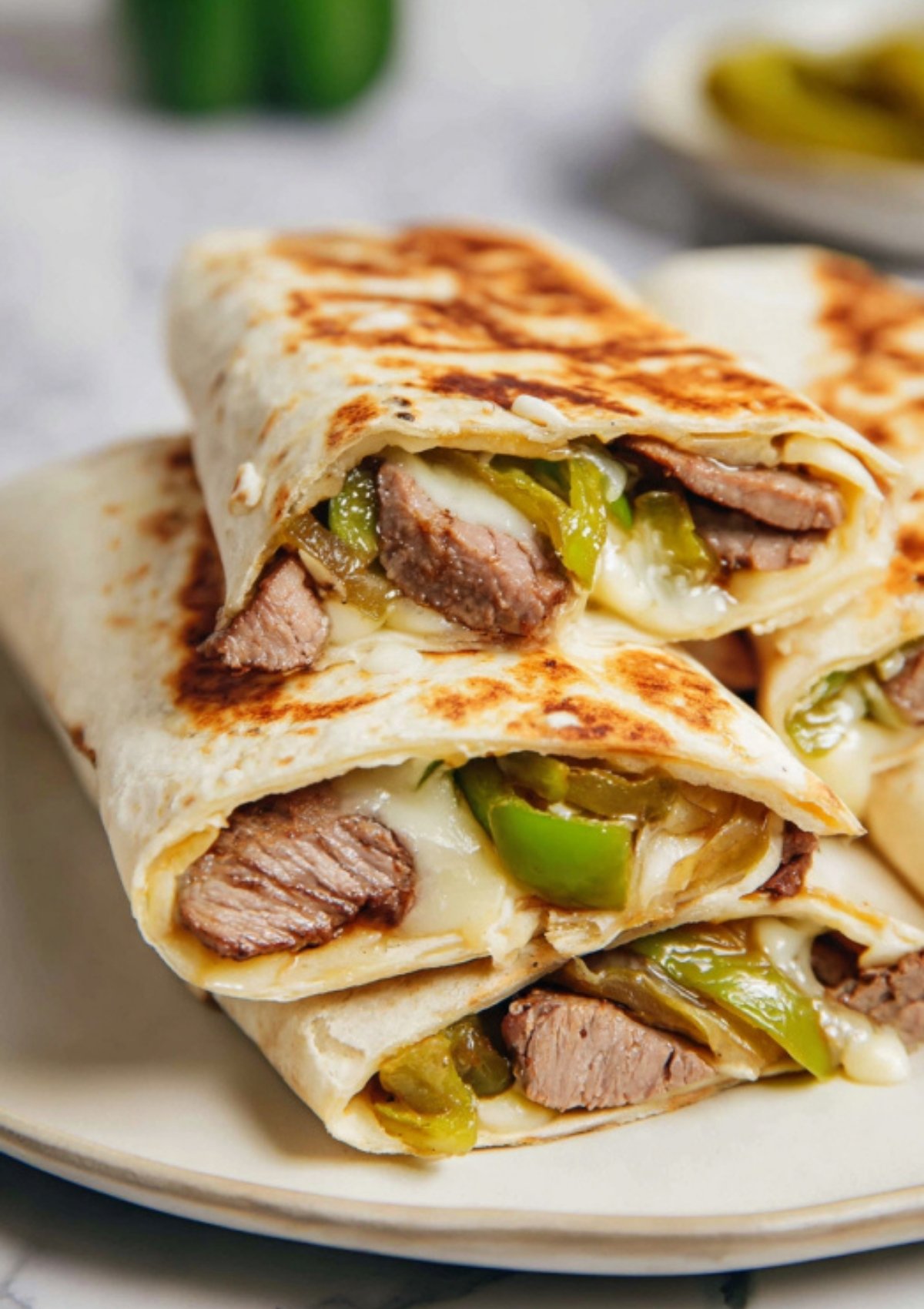 Close-up of Philly cheesesteak wraps sliced and stacked on a plate, with cheese and peppers peeking out.