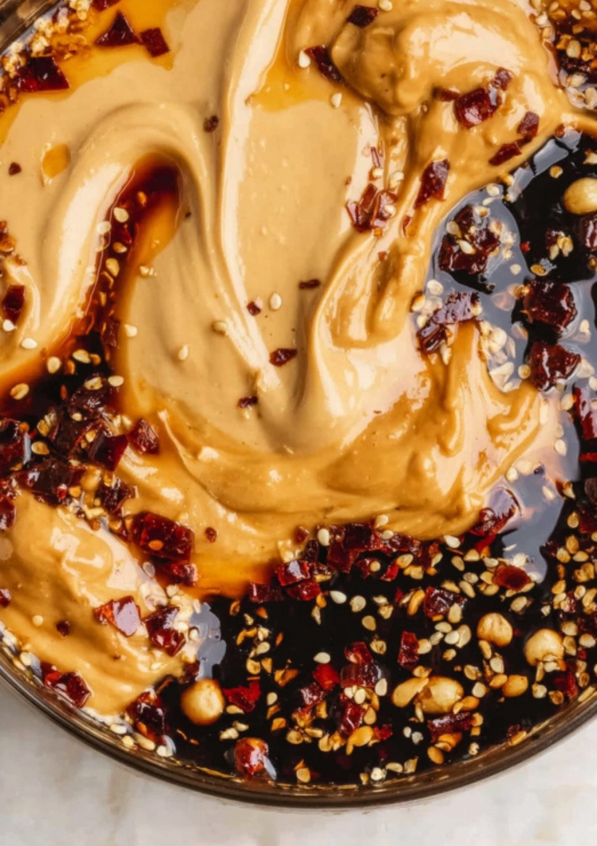 Close-up of creamy peanut butter mixed with chili flakes, sesame seeds, and soy sauce for Thai peanut noodles.