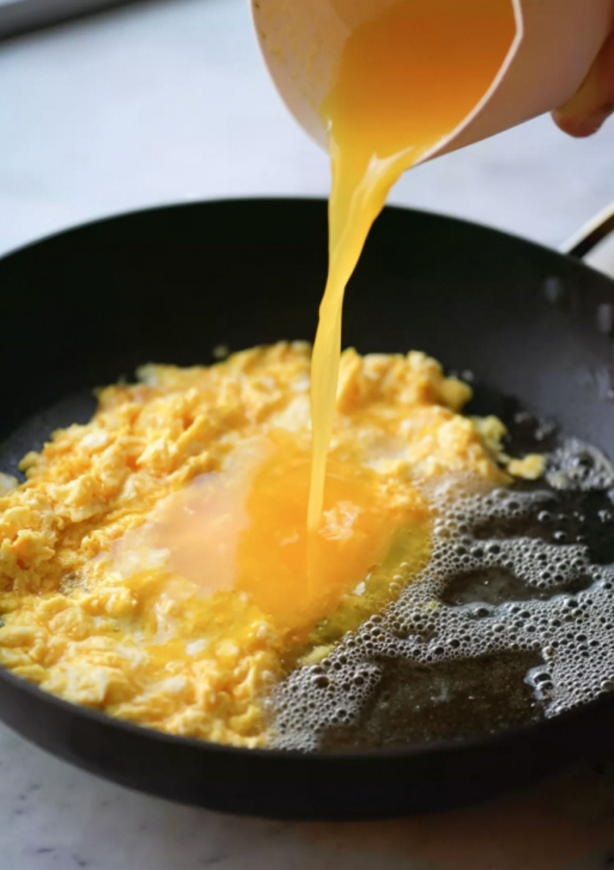 Whisked eggs poured into a skillet to scramble, prepping for authentic chicken fried rice.