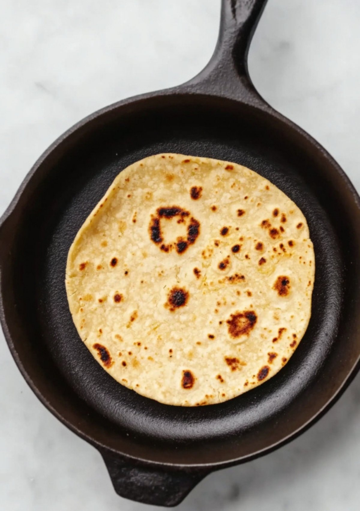 Corn tortilla warming in a cast iron skillet, showing golden brown spots, perfect base for crispy fish tacos and homemade taco nights.