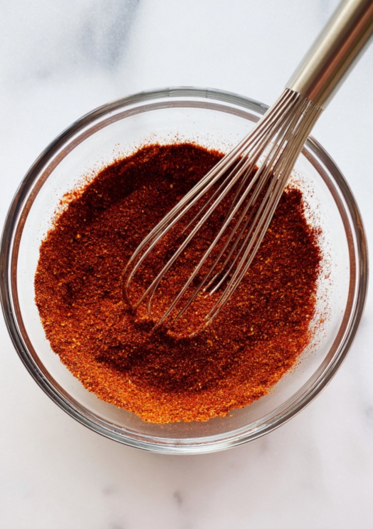 Glass bowl of vibrant, homemade fajita spice mix with a whisk, ideal for Tex-Mex chicken, pasta, or grilling.