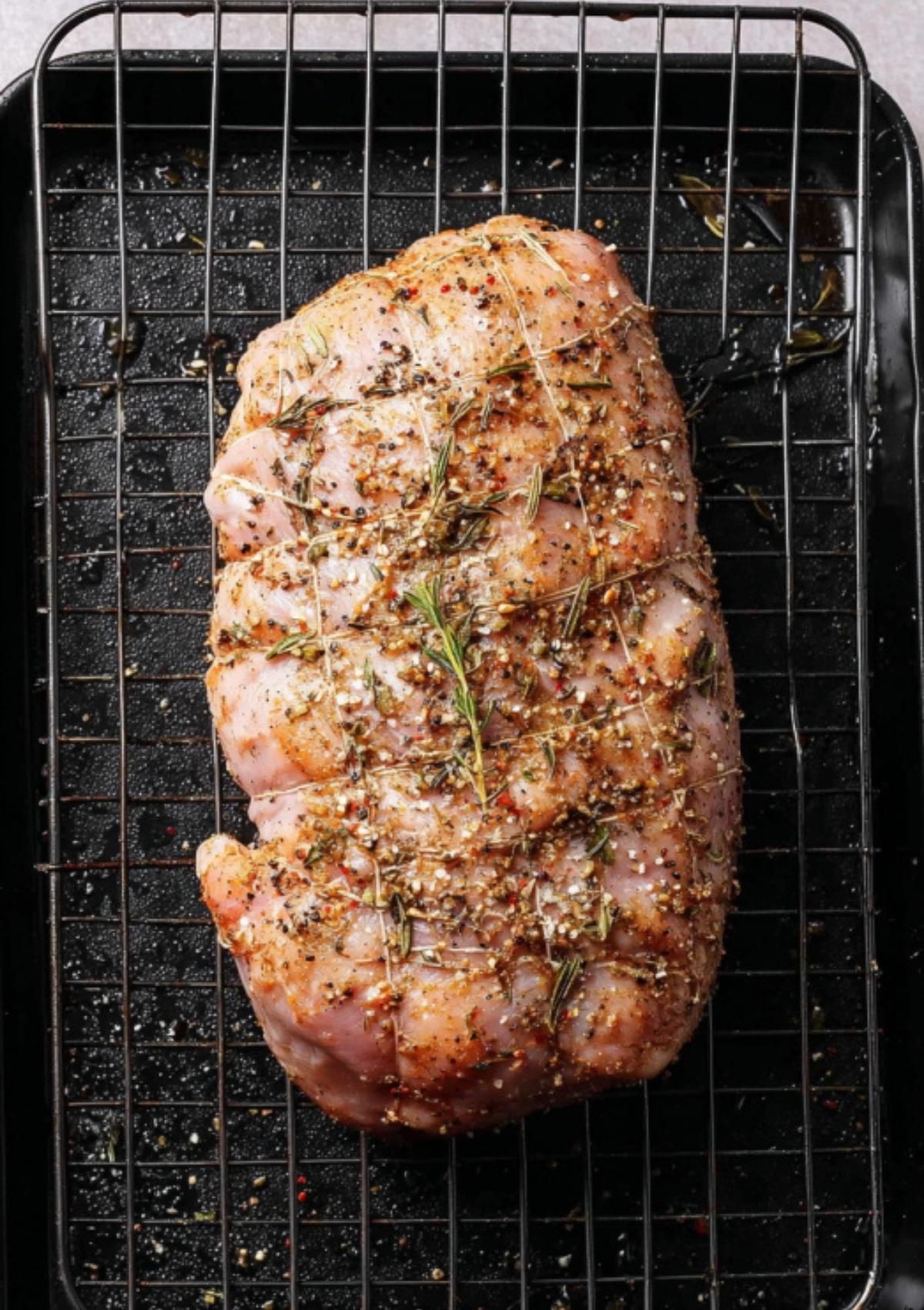 Uncooked Butterball turkey breast roast coated with herbs on a rack before baking.