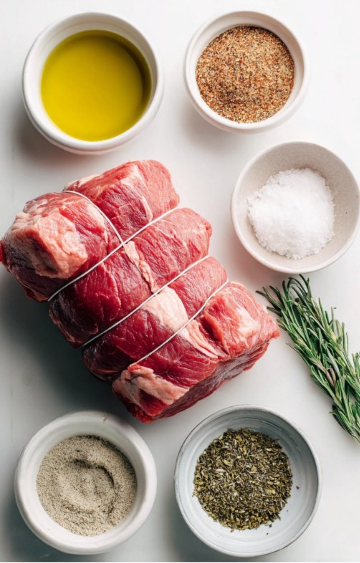 All the ingredients for sirloin tip roast: beef, olive oil, herbs, and seasonings on a white background