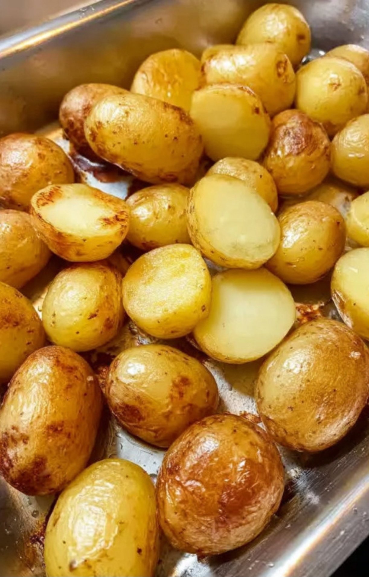 Tray of golden brown roasted baby potatoes, halved for extra crispiness, ideal for serving with roasted zucchini or any main dish.