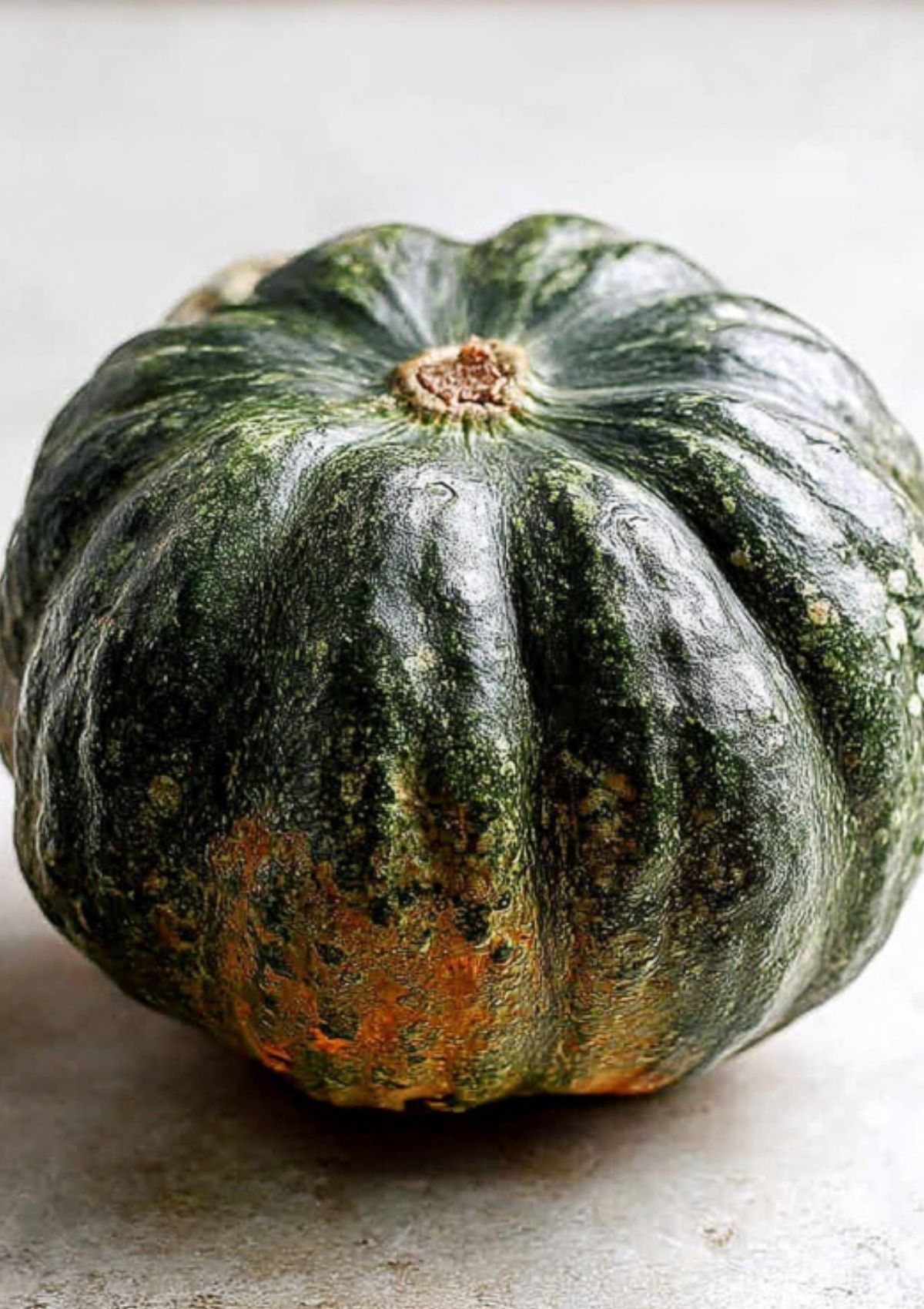 A whole kabocha squash with dark green, slightly textured skin and a touch of orange, ready to be sliced and roasted.
