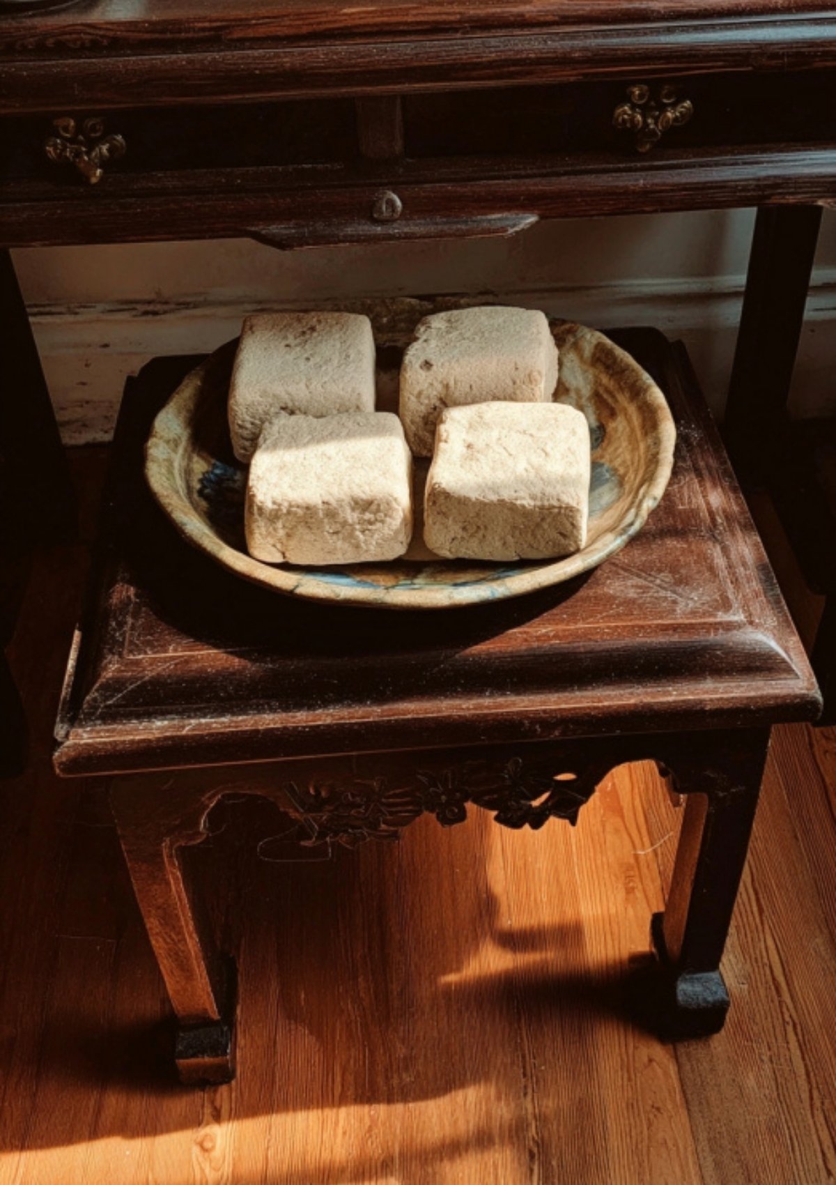 Four finished meju blocks resting in a rustic bowl on a small wooden table, ready to be used for homemade soy sauce.
