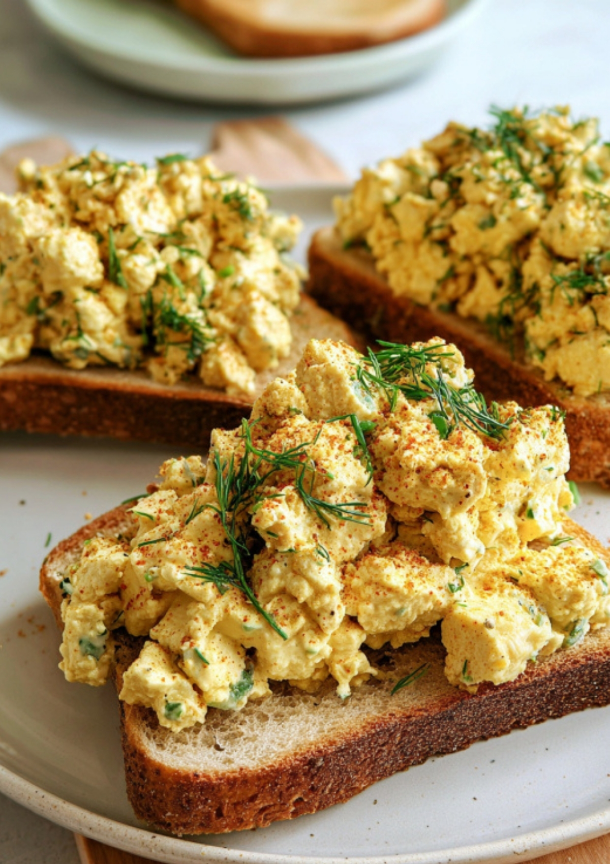 Generous scoops of tofu egg salad piled onto slices of toasted bread, topped with dill and paprika for a colorful, high-protein vegan lunch.