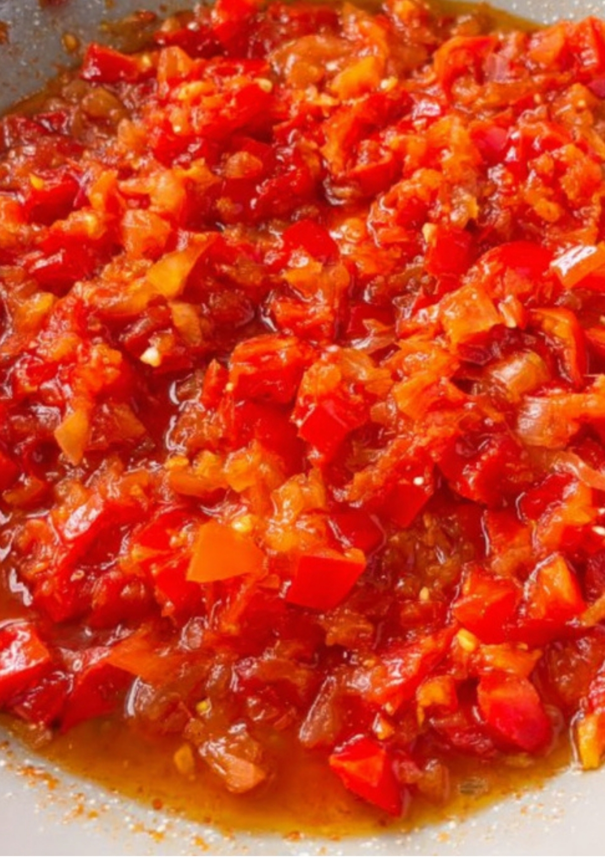 Chopped tomatoes and red peppers simmering in oil, forming the flavorful base for Nigerian egg sauce.