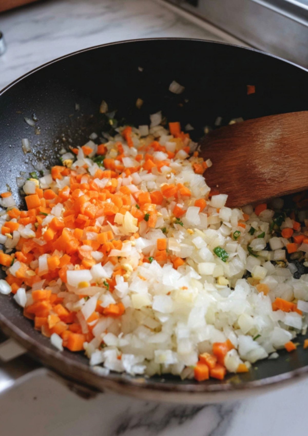Chopped onions and carrots sizzling in a skillet, starting a fresh batch of chicken fried rice.