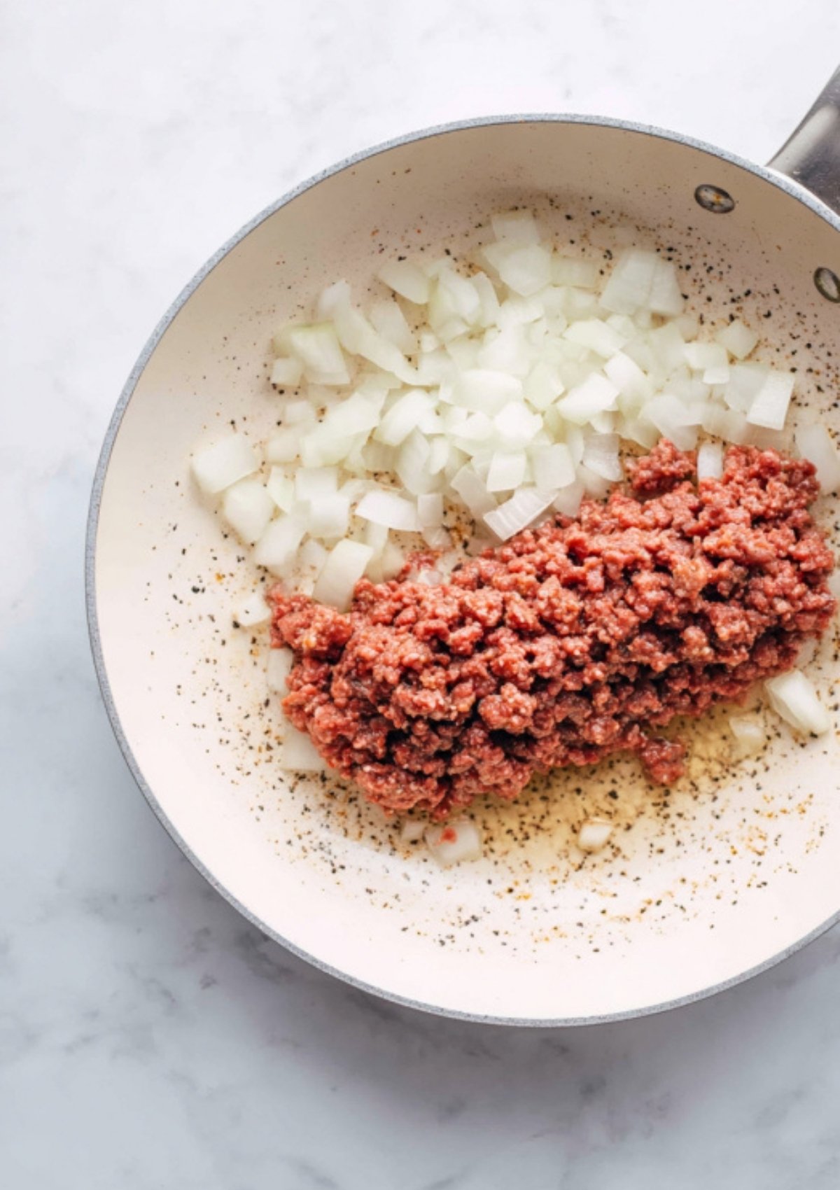 Raw ground beef and chopped onions cooking in a skillet as the first step to homemade Sloppy Joe Stuffed Peppers.