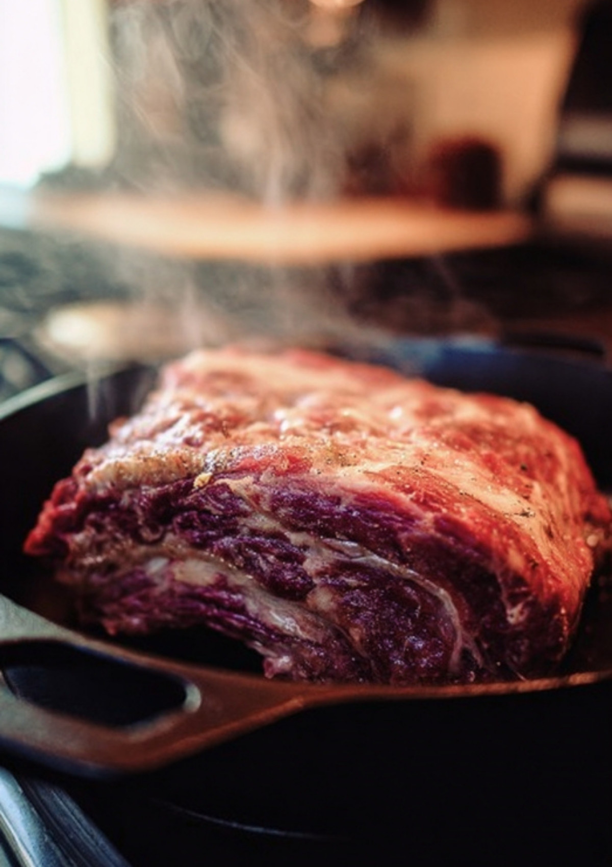 Prime rib roast searing in a cast iron skillet with steam rising, building flavor for a perfect crust