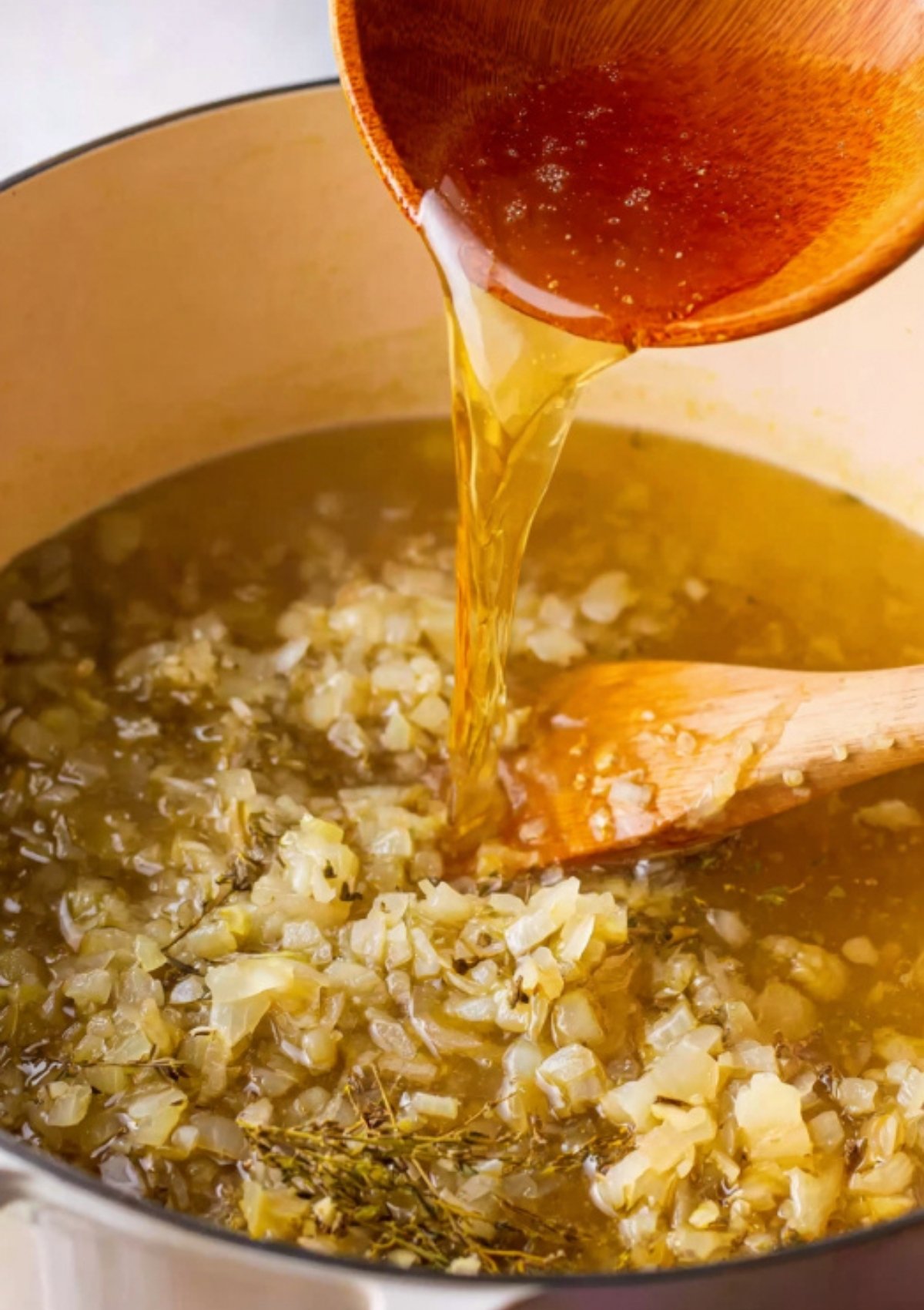 Broth being poured into a pot with onions and Italian herbs, building the base for creamy tomato tortellini soup.
