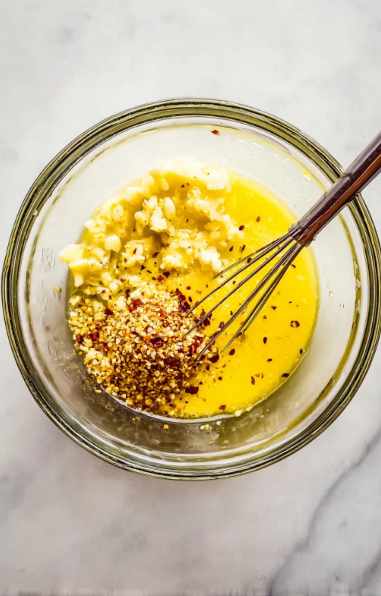 Garlic, mustard, honey, and spices being whisked together in a glass bowl to make a flavorful chicken marinade