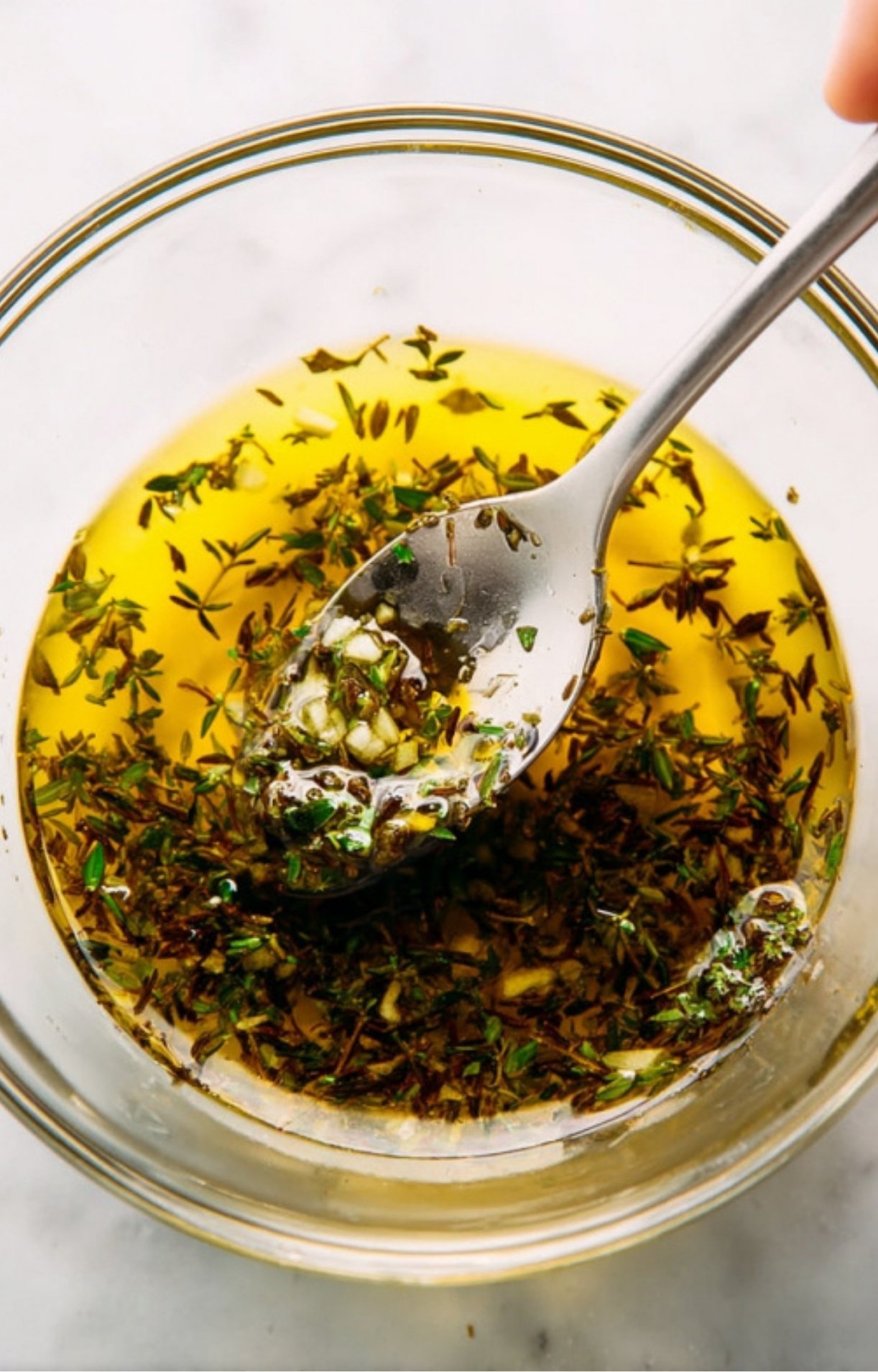 Closeup of olive oil, fresh thyme, and garlic marinade in a bowl, the best way to add flavor to roast beef recipes.
