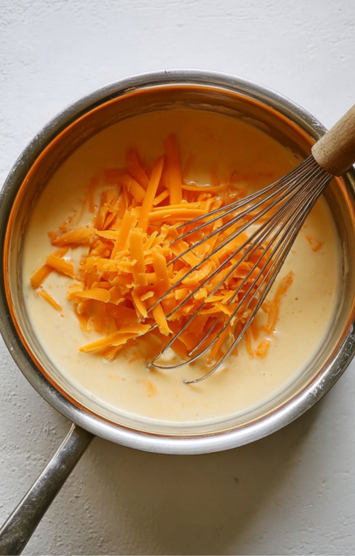 Shredded cheddar cheese being mixed into a pot of sauce for an easy homemade cheese sauce