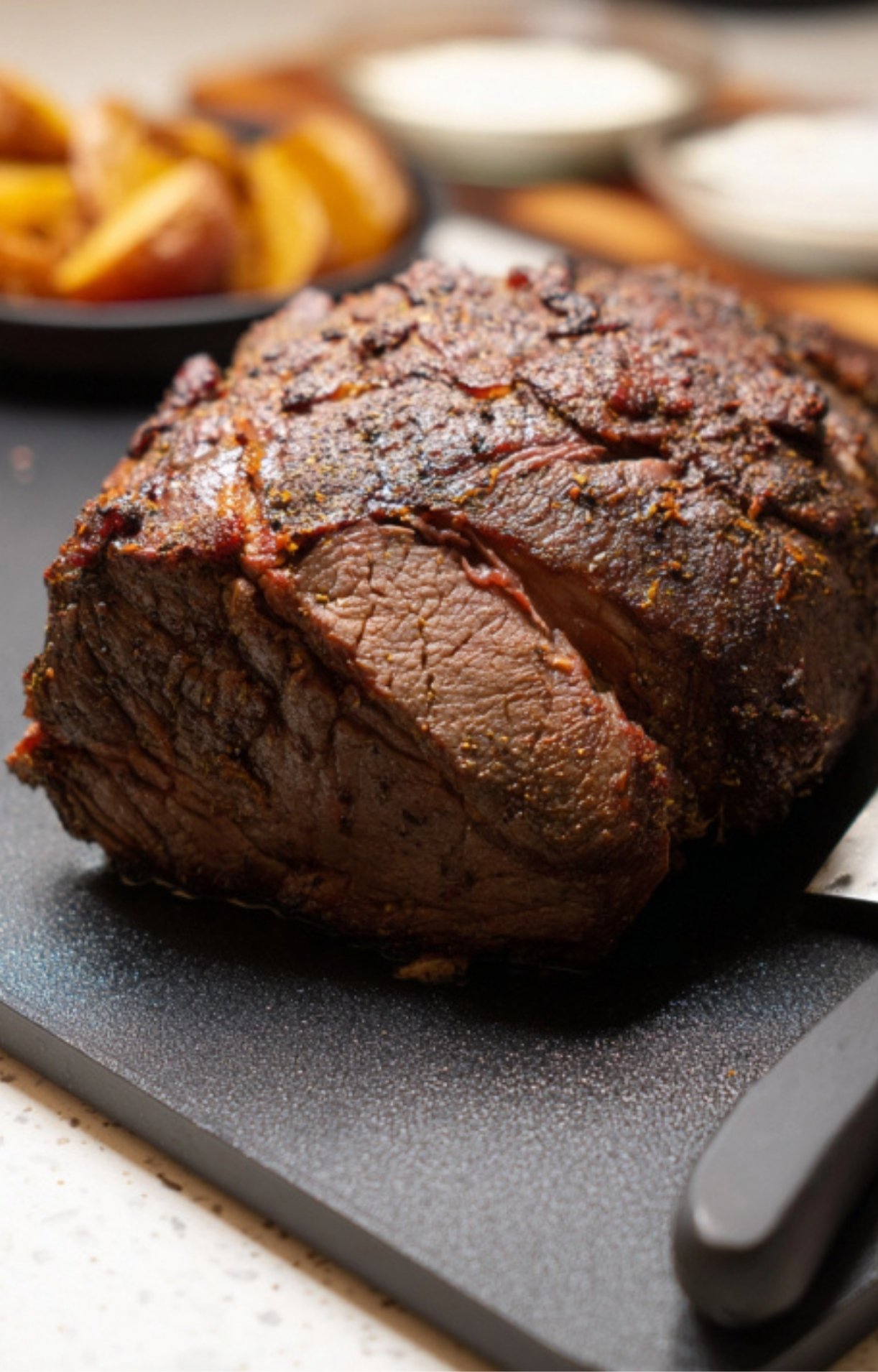 Whole seasoned roast beef resting on a black cutting board, juicy and perfectly cooked for slicing at Sunday roast.
