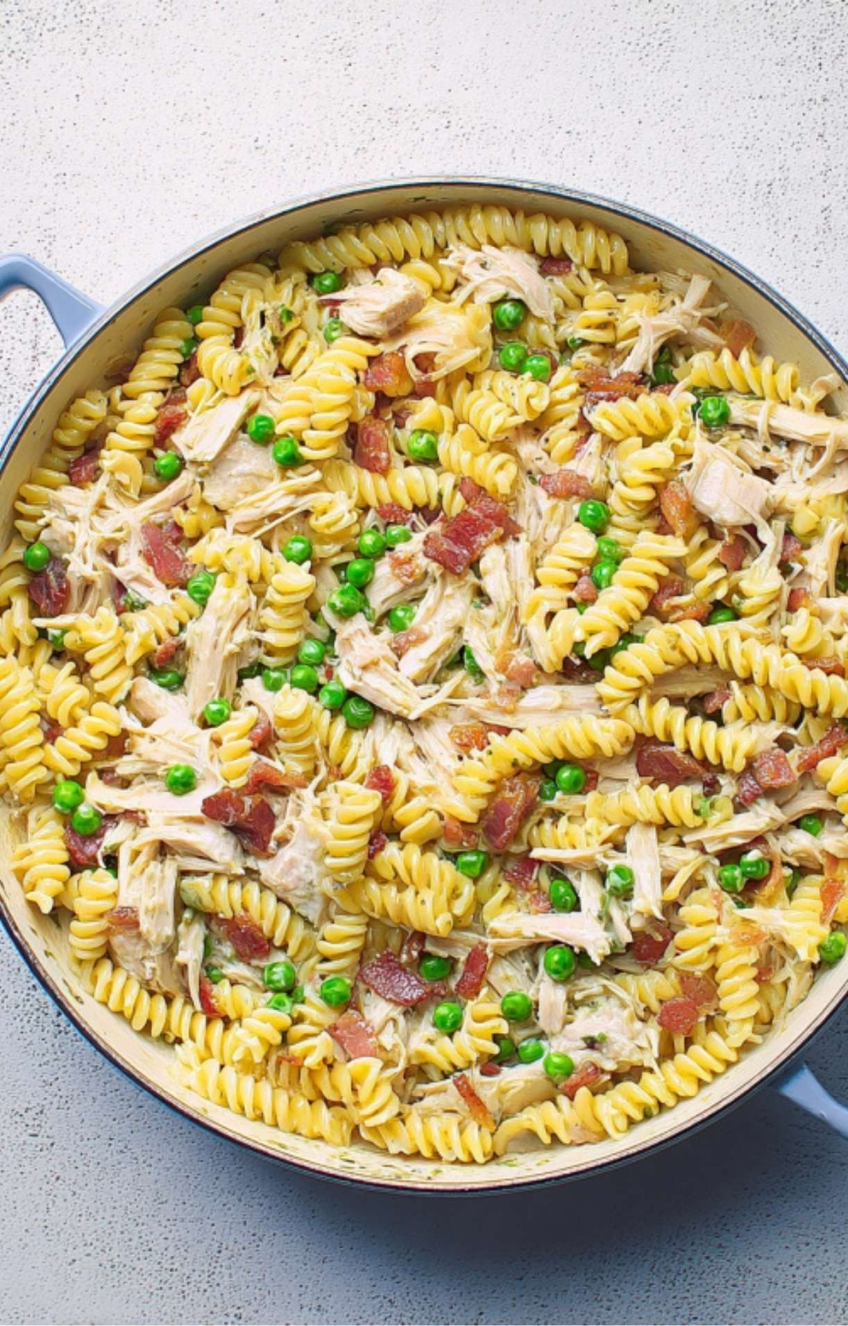 Overhead shot of a large skillet filled with fusilli pasta, shredded chicken, peas, and bacon in a creamy sauce.