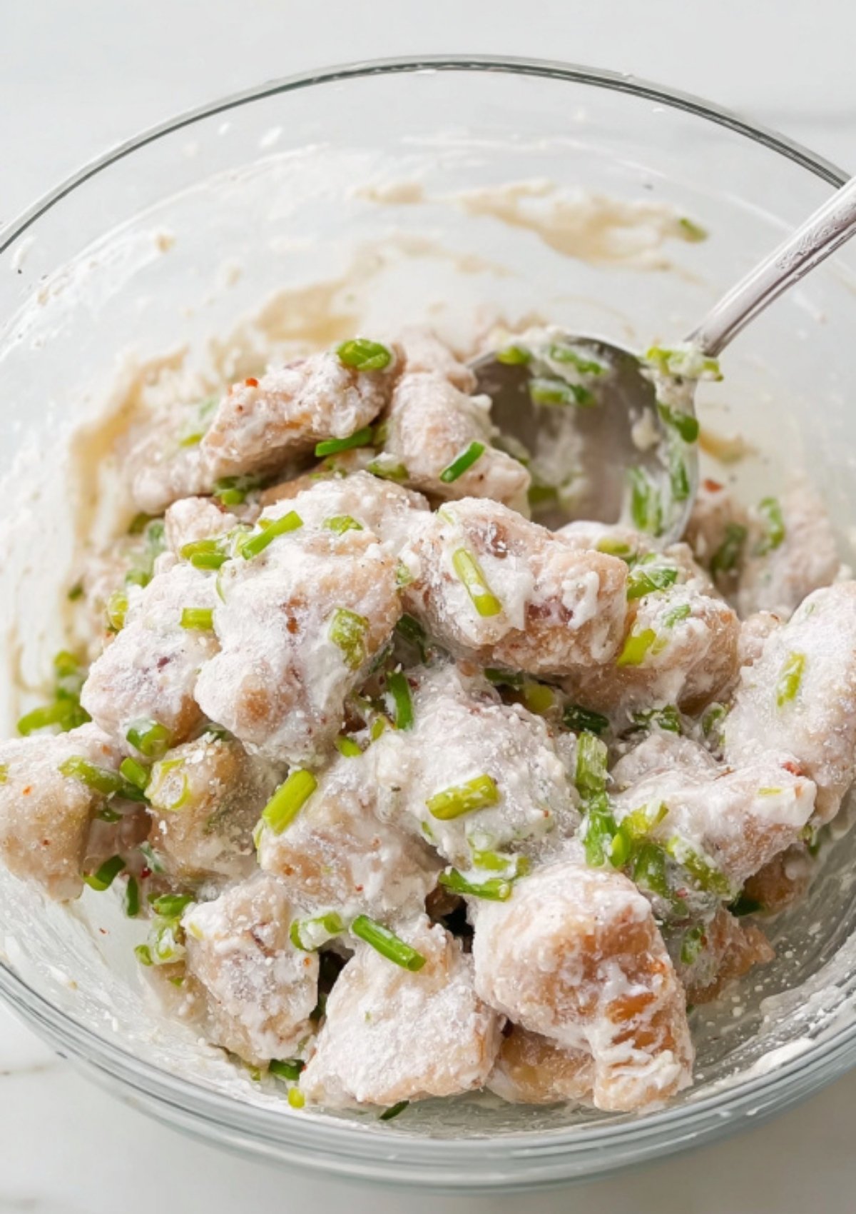 Cubed pork pieces coated in marinade and cornstarch in a glass bowl, ready for frying.