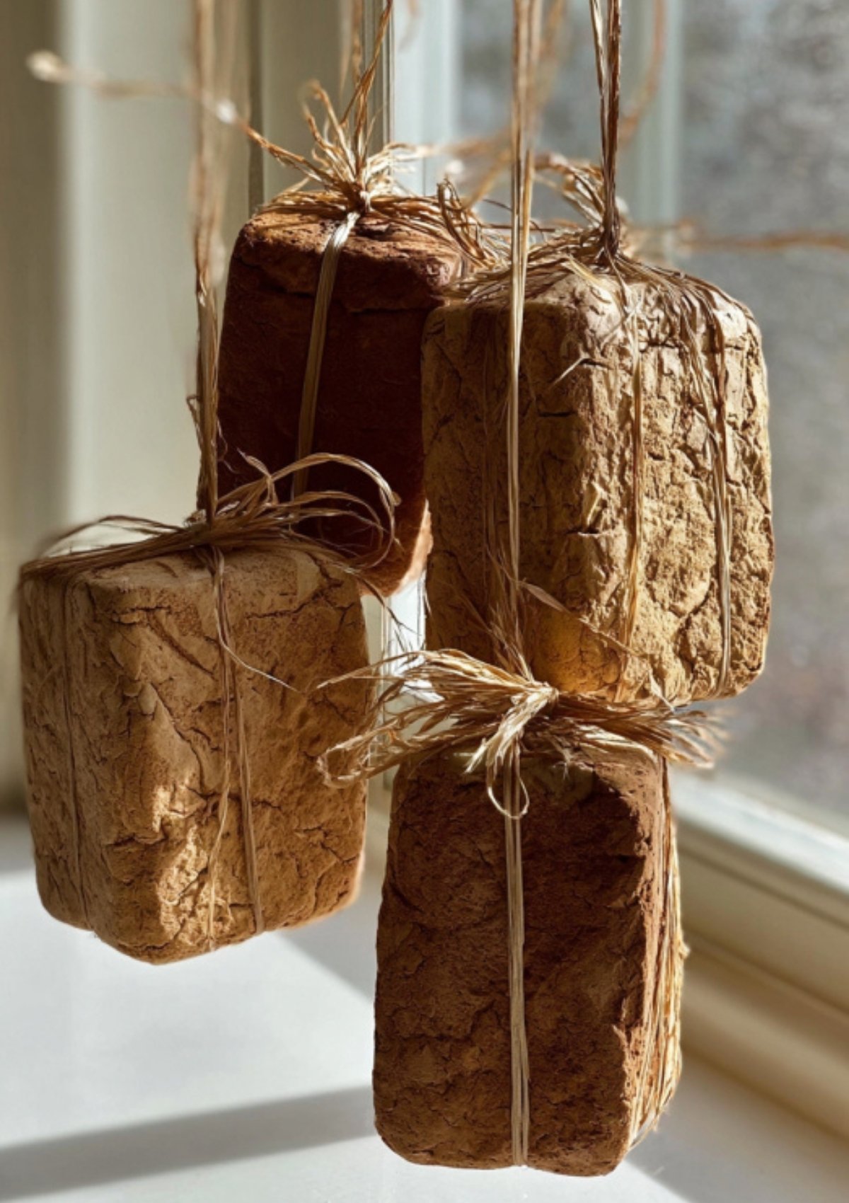 Several meju blocks tied with twine, hanging by a sunny window to air dry and cure before the soy sauce fermentation process.
