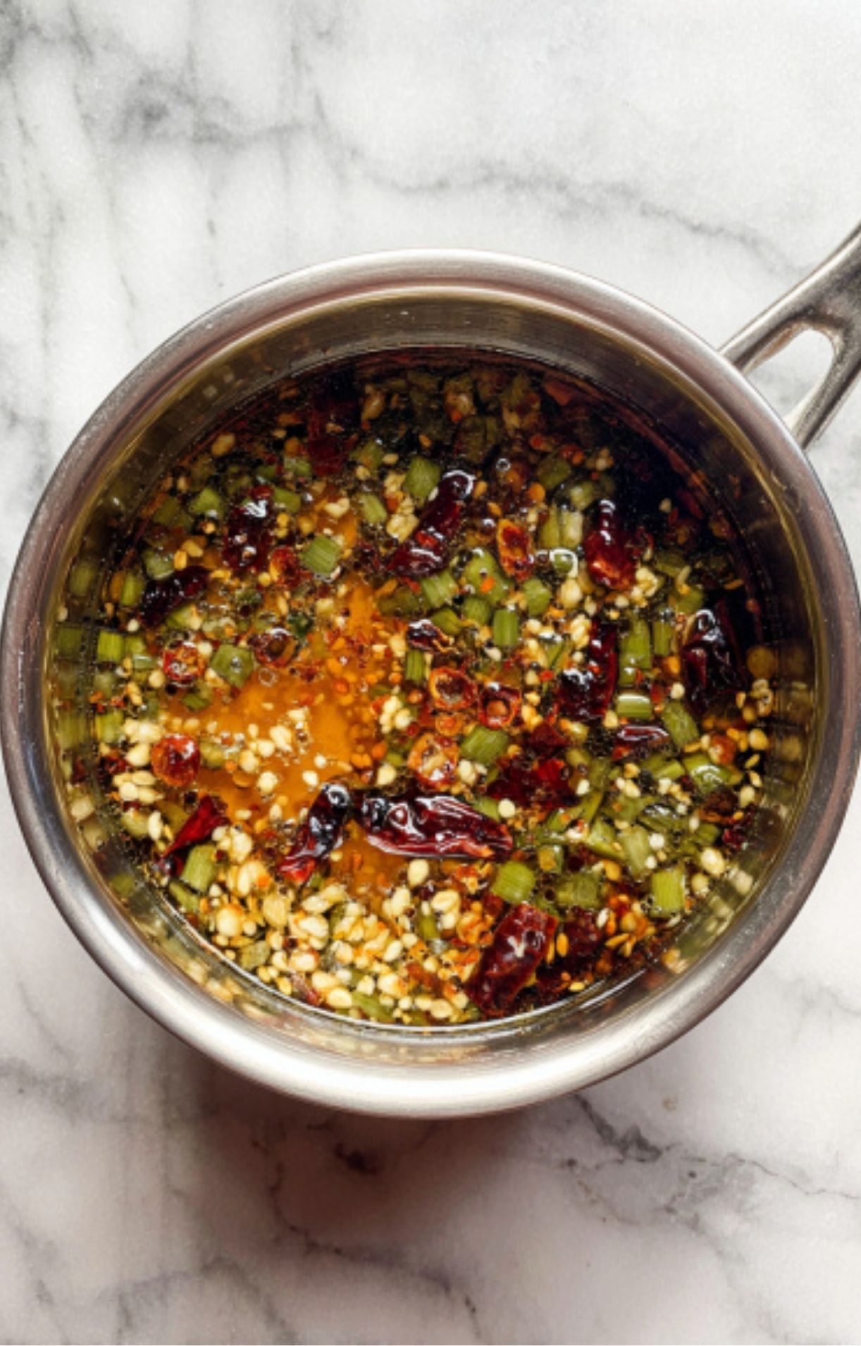 Aromatics and spices simmering in oil in a saucepan to infuse flavor for homemade Asian chili sauce.
