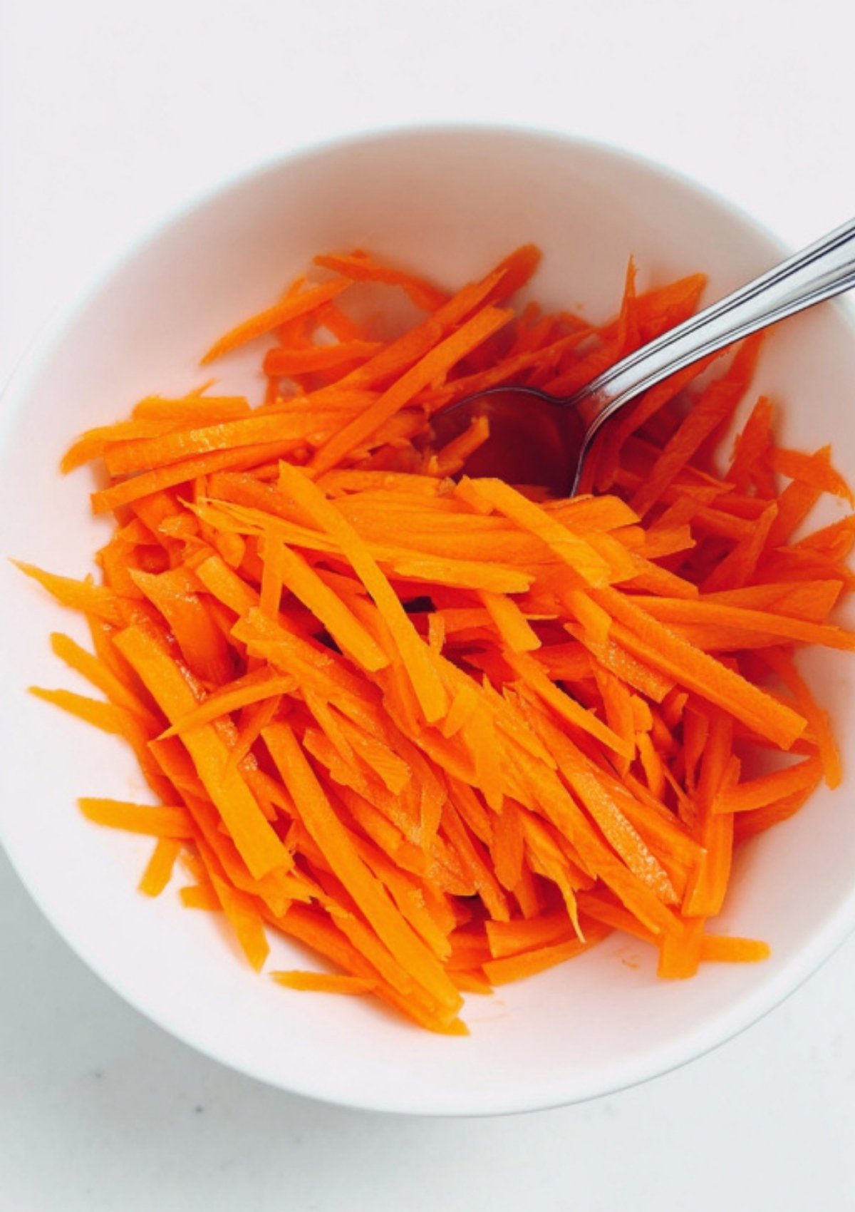 White bowl filled with julienned carrots, perfect topping for homemade spicy tuna rice bowls.