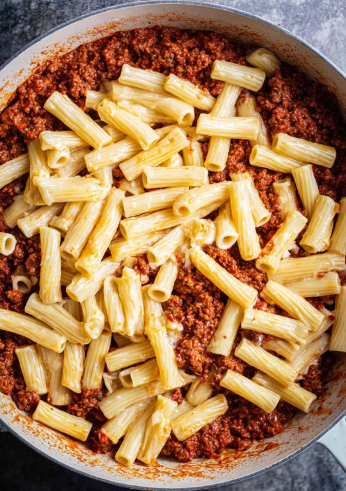 Cooked ziti pasta mixed with homemade meat sauce in a skillet.