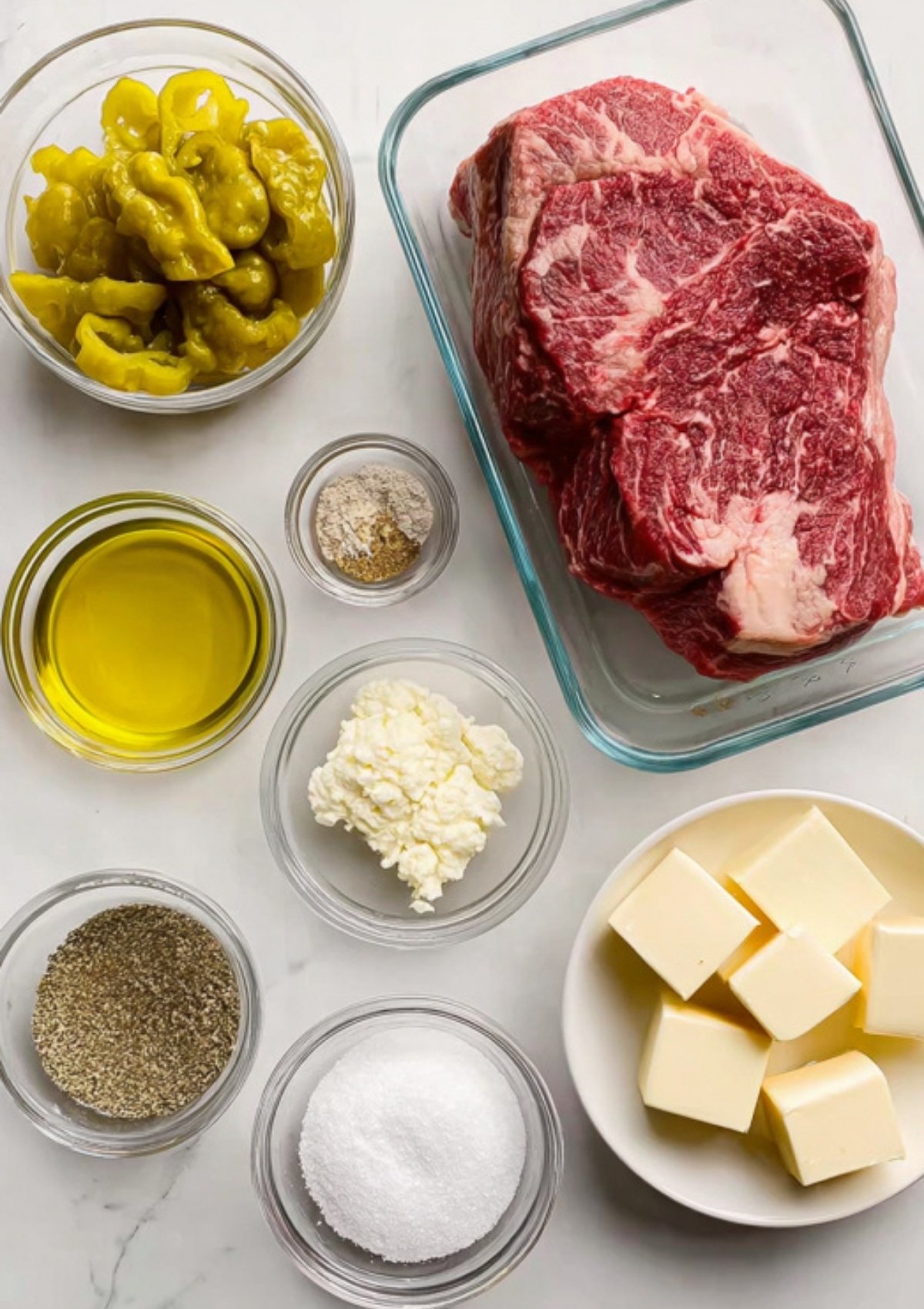 Flat lay of classic Mississippi pot roast ingredients including chuck roast, pepperoncini, butter, ranch mix, au jus mix, and seasonings.