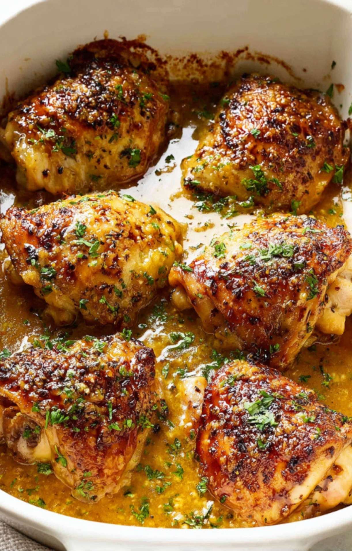 Cooked chicken thighs in white baking dish with golden, caramelized glaze and parsley, fresh from the oven