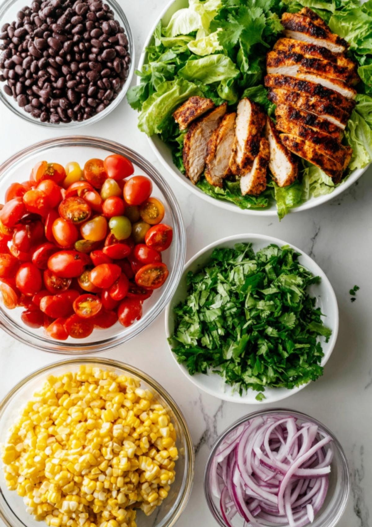 Bowls of chopped romaine, black beans, grilled chicken, tomatoes, corn, cilantro, and red onion for assembling Southwest Chicken Salad