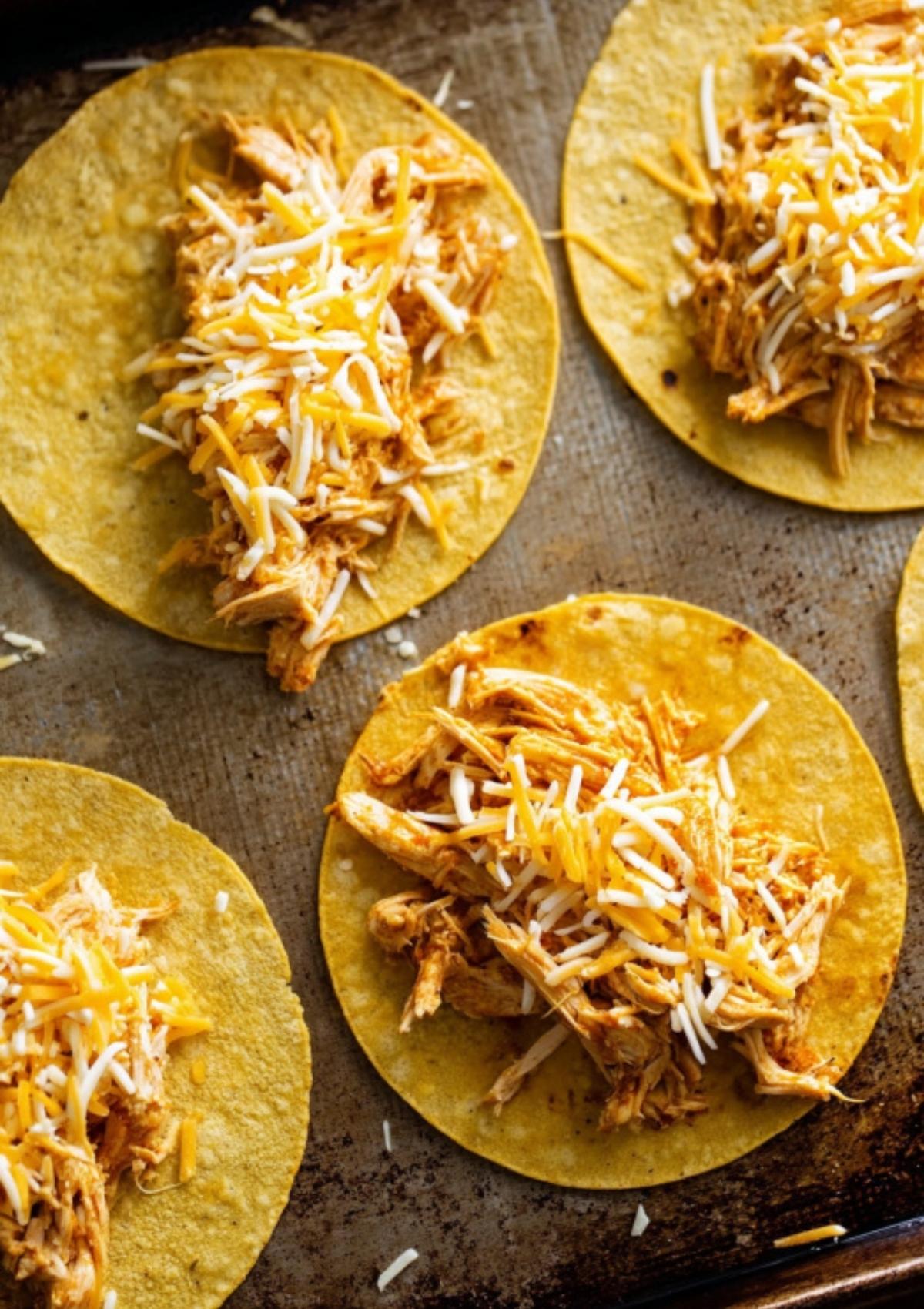 Corn tortillas filled with shredded buffalo chicken and melted cheese on a baking sheet before baking.