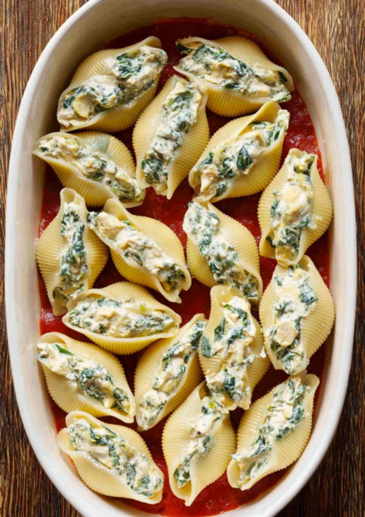 Jumbo pasta shells stuffed with a creamy chicken and spinach filling, placed in a baking dish over red pasta sauce, ready for baking.