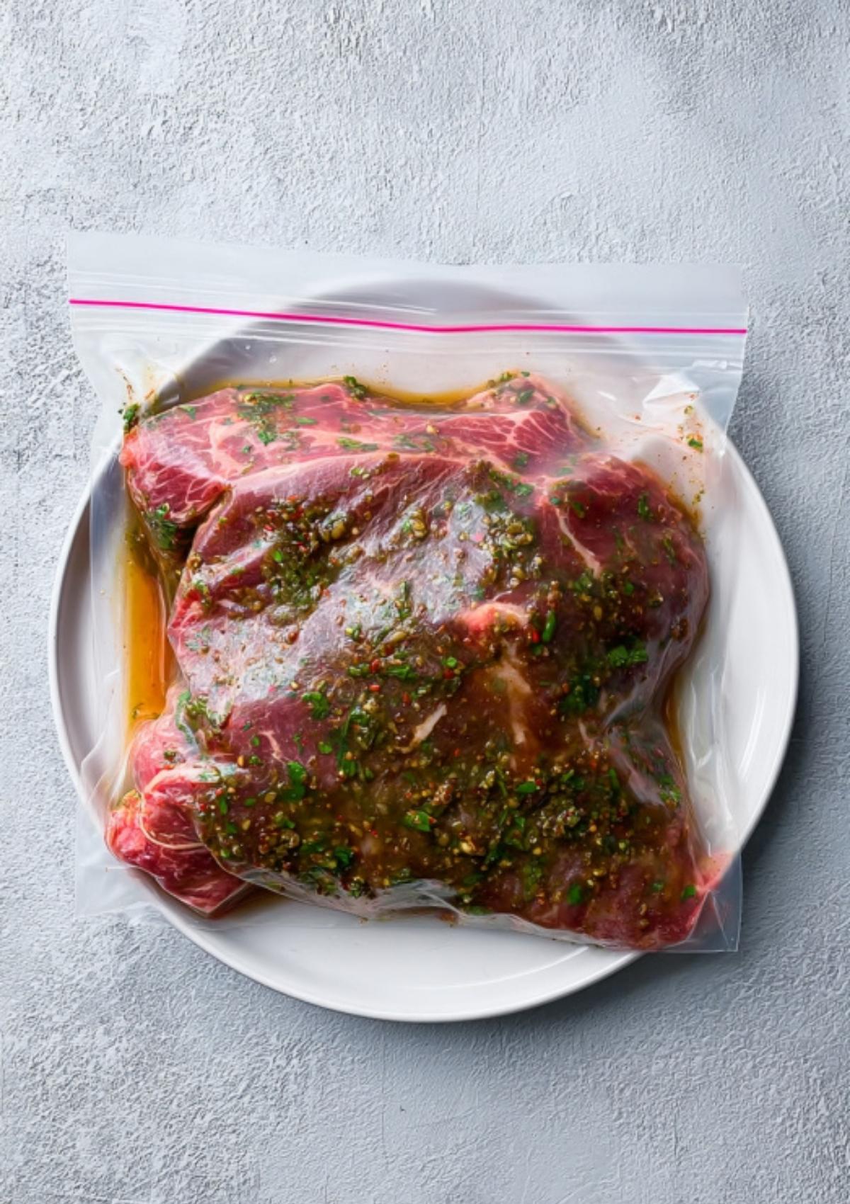 Chuck roast marinating in a zip-top bag with herbs and spices—essential prep for juicy grilled roast beef.
