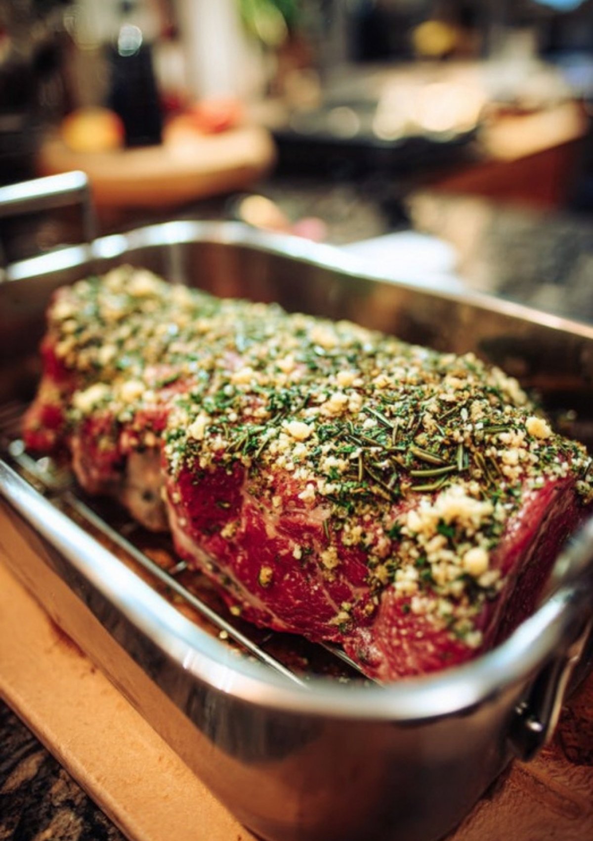 Uncooked prime rib roast coated with fresh herbs and garlic in a roasting pan, prepped for baking