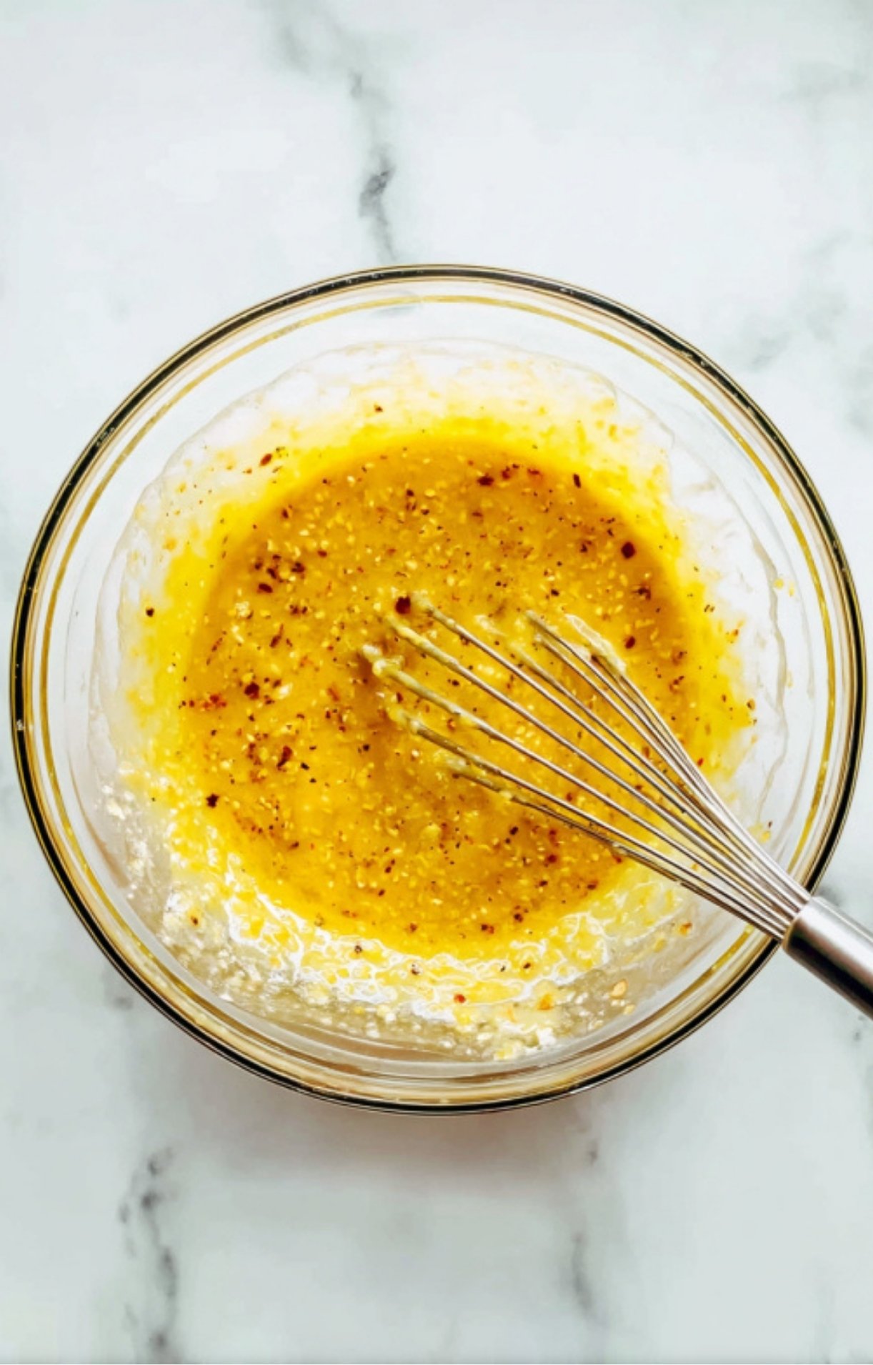 Glass bowl with whisk and golden honey mustard sauce for baked chicken thighs, showing a simple homemade glaze