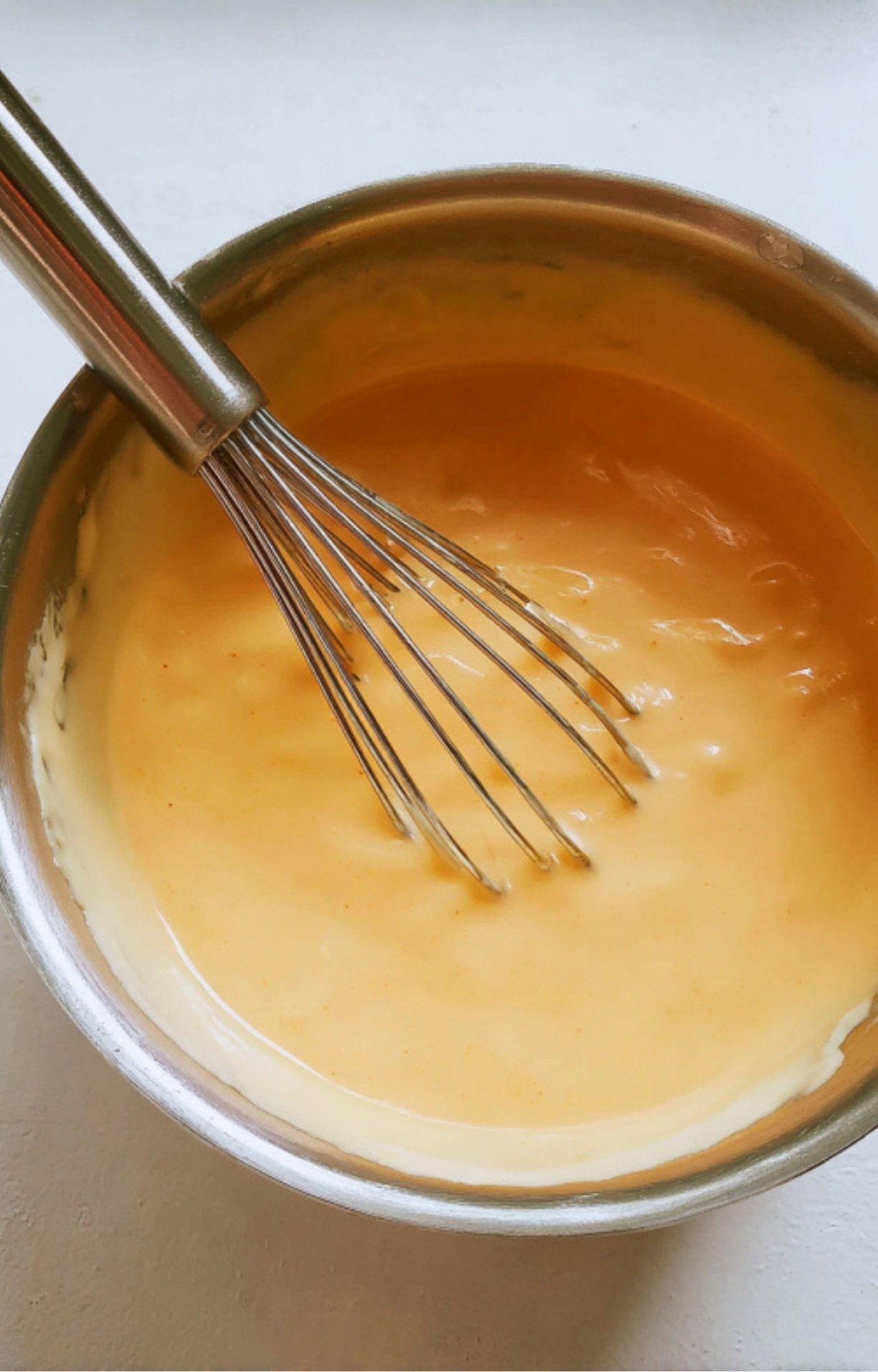 Smooth and creamy cheddar cheese sauce in a mixing bowl with a whisk