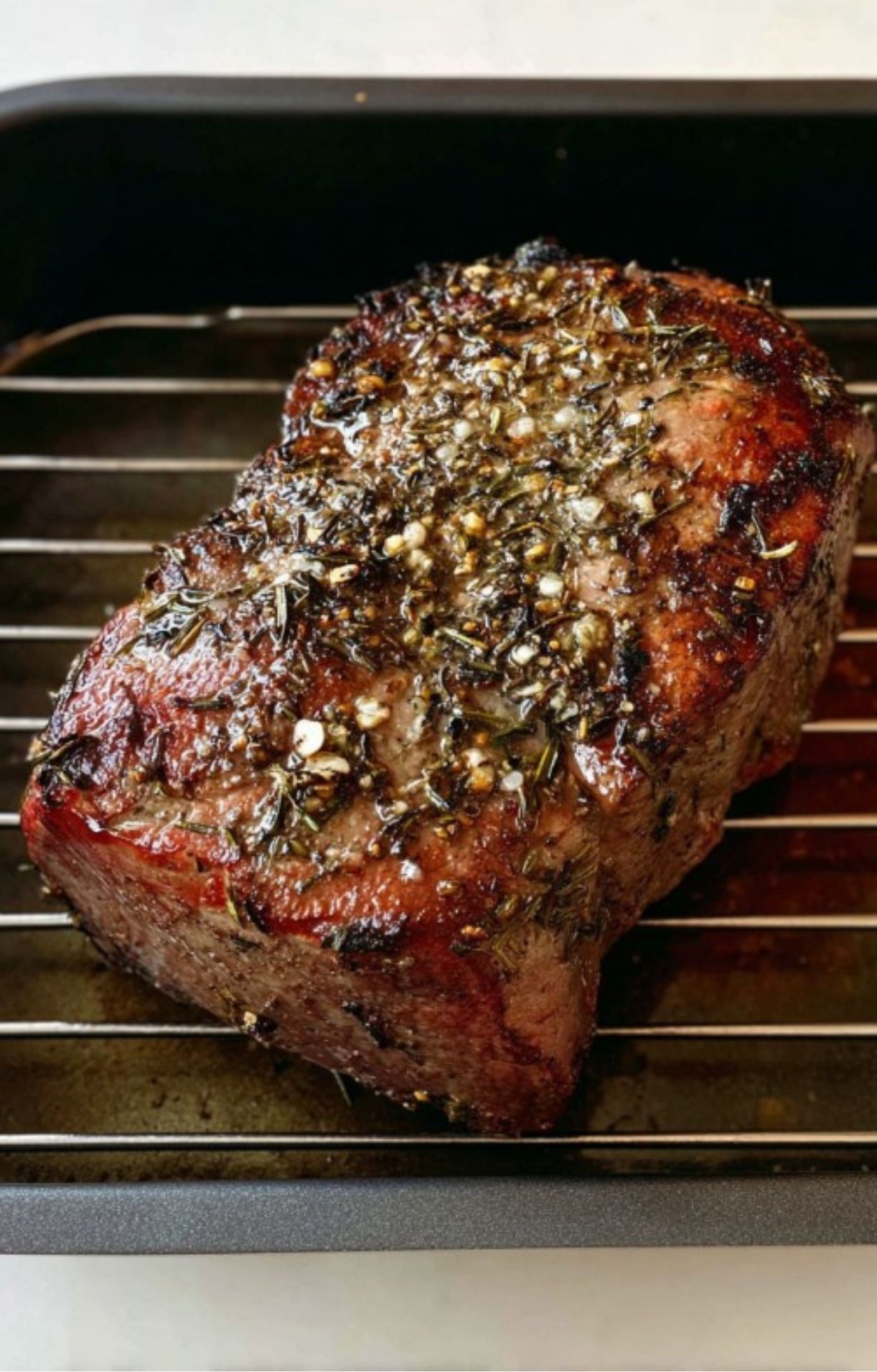 Whole beef roast with a golden brown herb crust on a rack, fresh from the oven