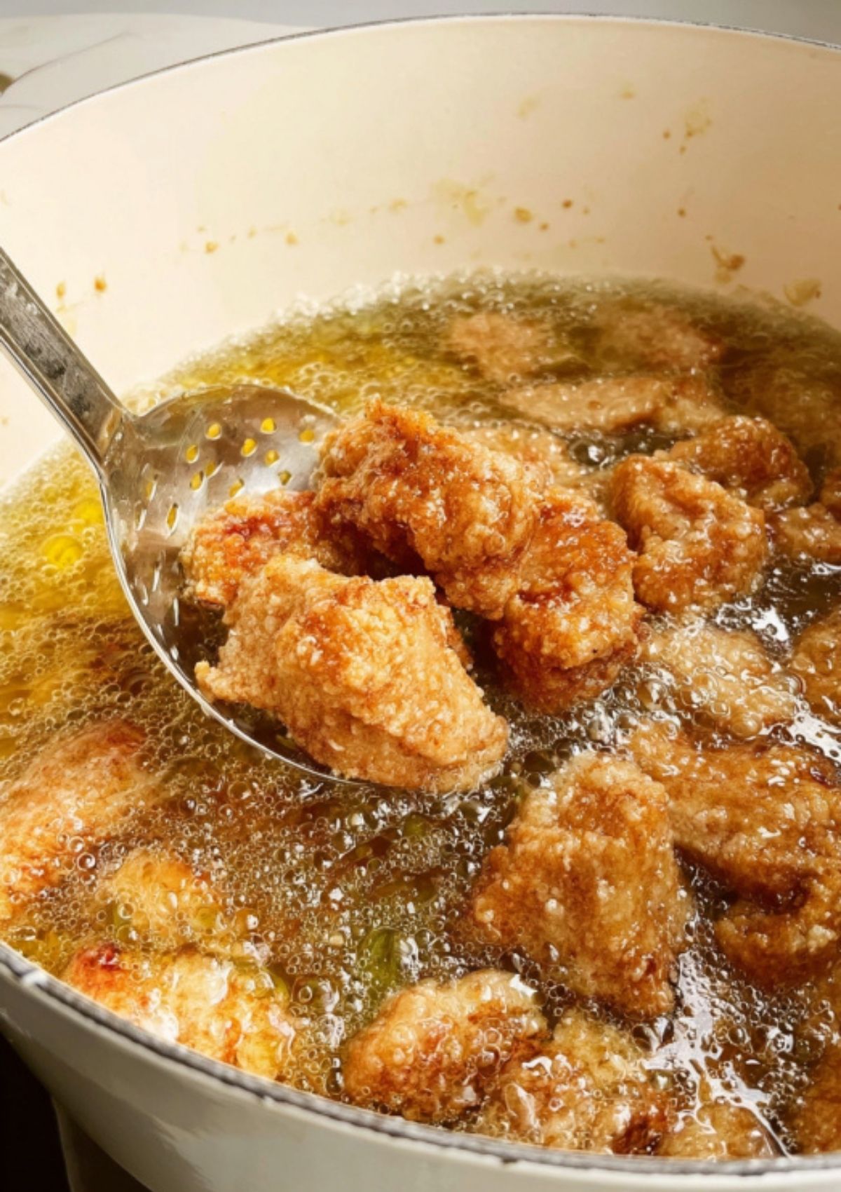 Crispy pork pieces being fried in hot oil with a slotted spoon for sweet and sour pork.