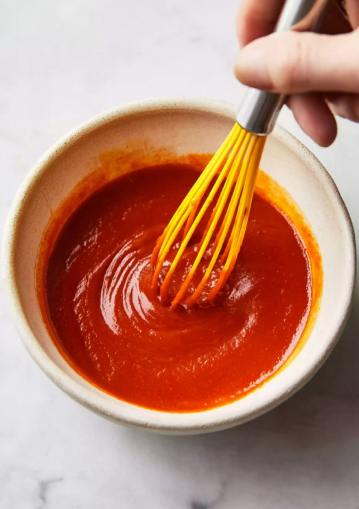 Hand whisking bright red gochujang sauce in a small bowl