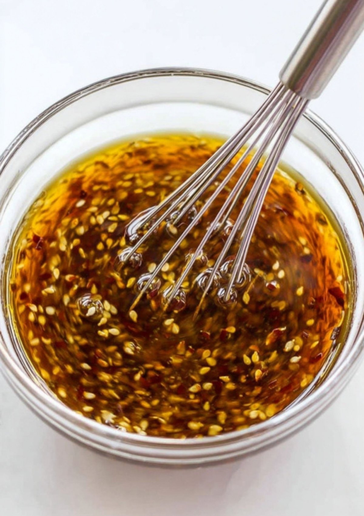 Soy ginger sauce being whisked in a clear bowl with sesame seeds and chili flakes. Ideal for marinades, salads, and clean eating recipes.