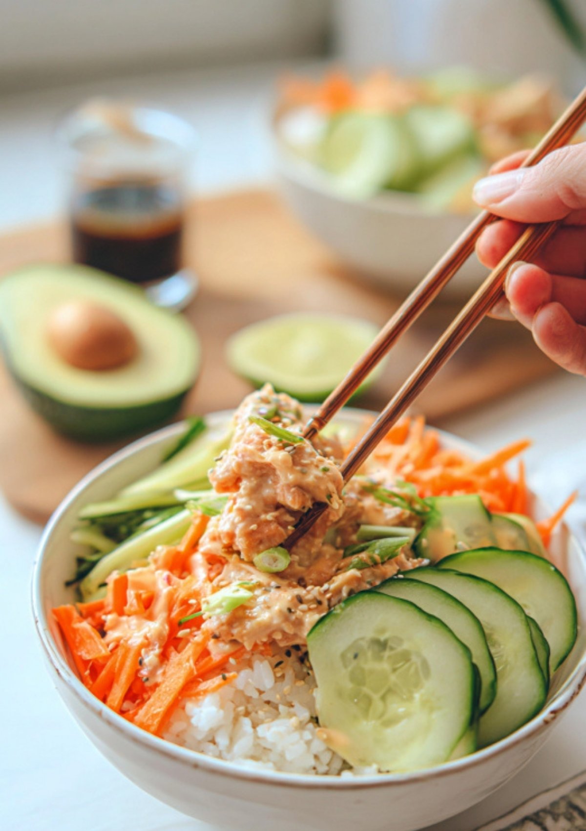 Close-up of a spicy tuna rice bowl with rice, spicy tuna, cucumber, carrots, and avocado being picked up with chopsticks.