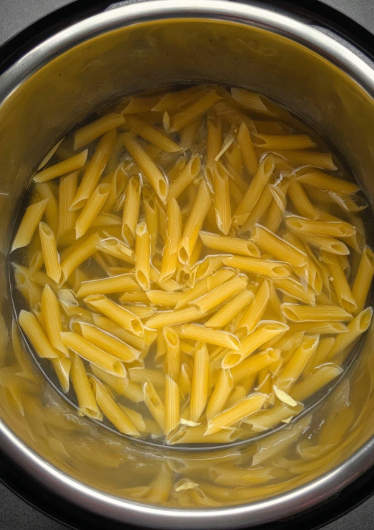 Ziti pasta boiling in a stainless steel pot filled with hot water.