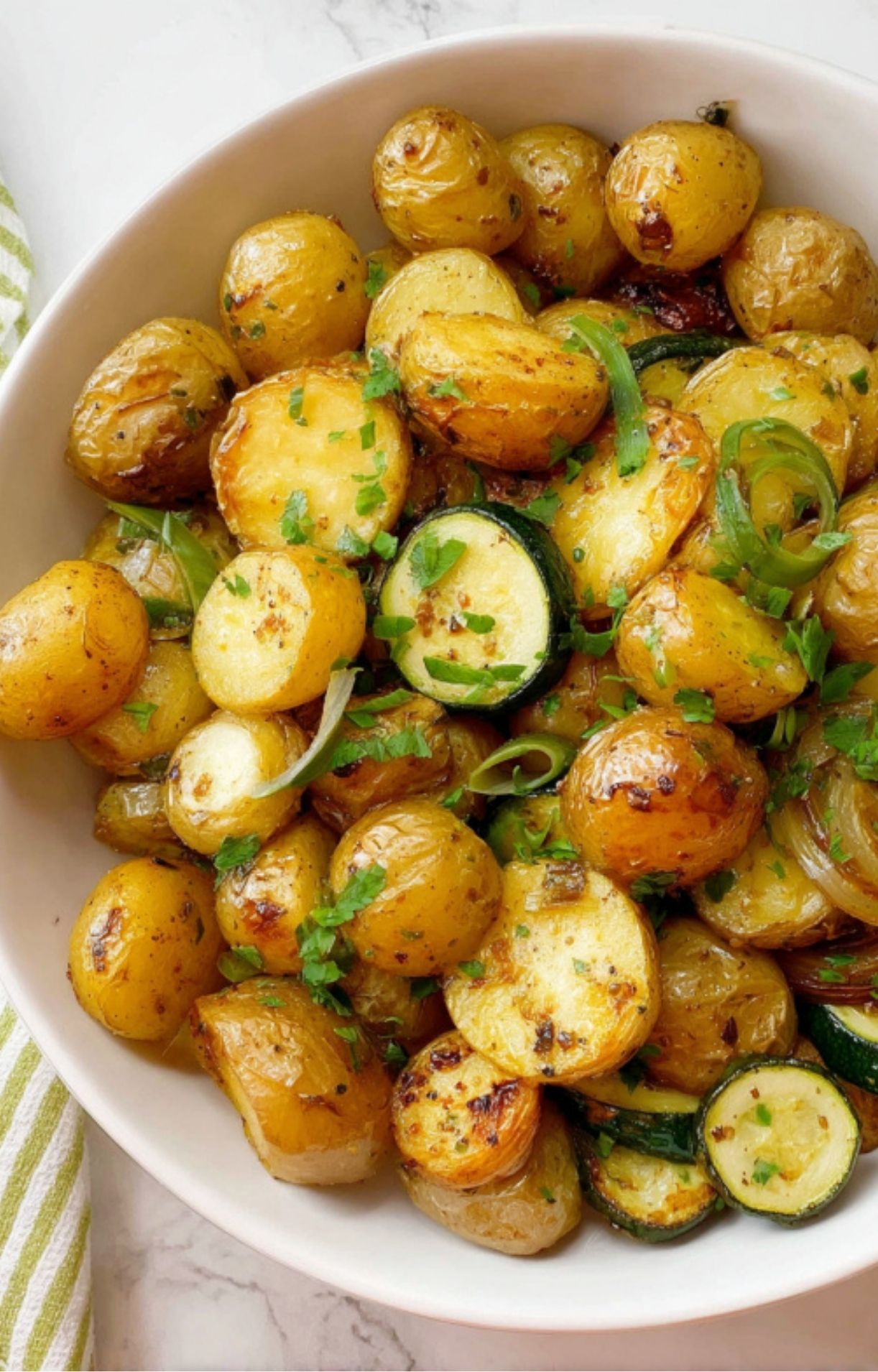 Serving bowl filled with roasted potatoes and zucchini, finished with fresh parsley and sliced green onions, perfect for weeknight or holiday meals.