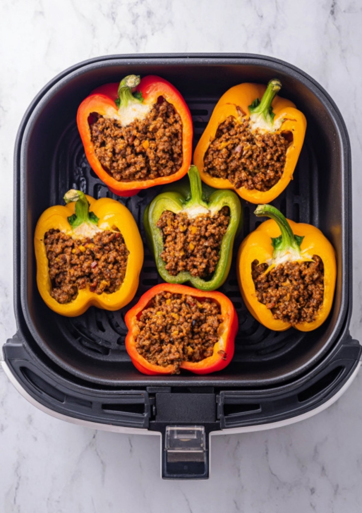 Halved red, yellow, and green bell peppers stuffed with Sloppy Joe filling arranged in an air fryer basket