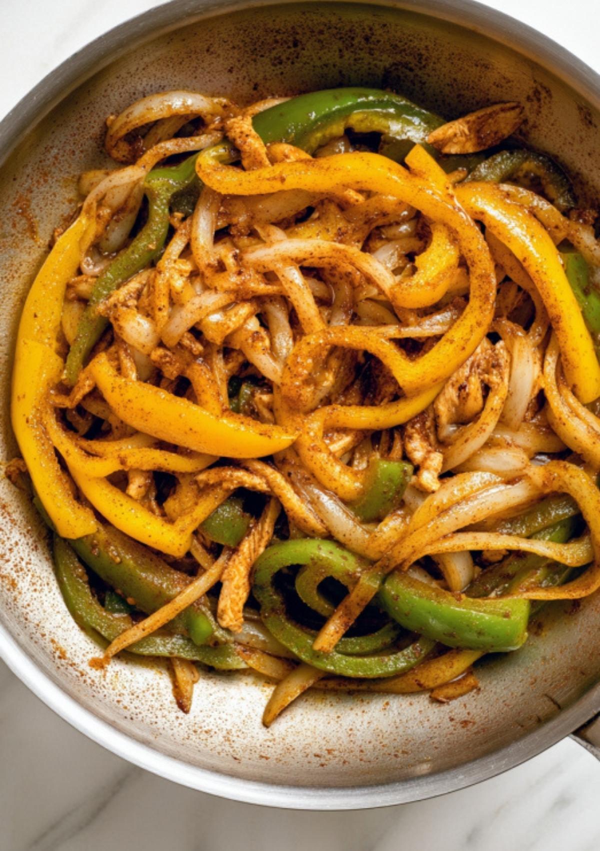 Yellow and green bell peppers with sliced onions sautéed with Tex-Mex spices in a skillet, perfect for adding flavor to creamy chicken pasta.