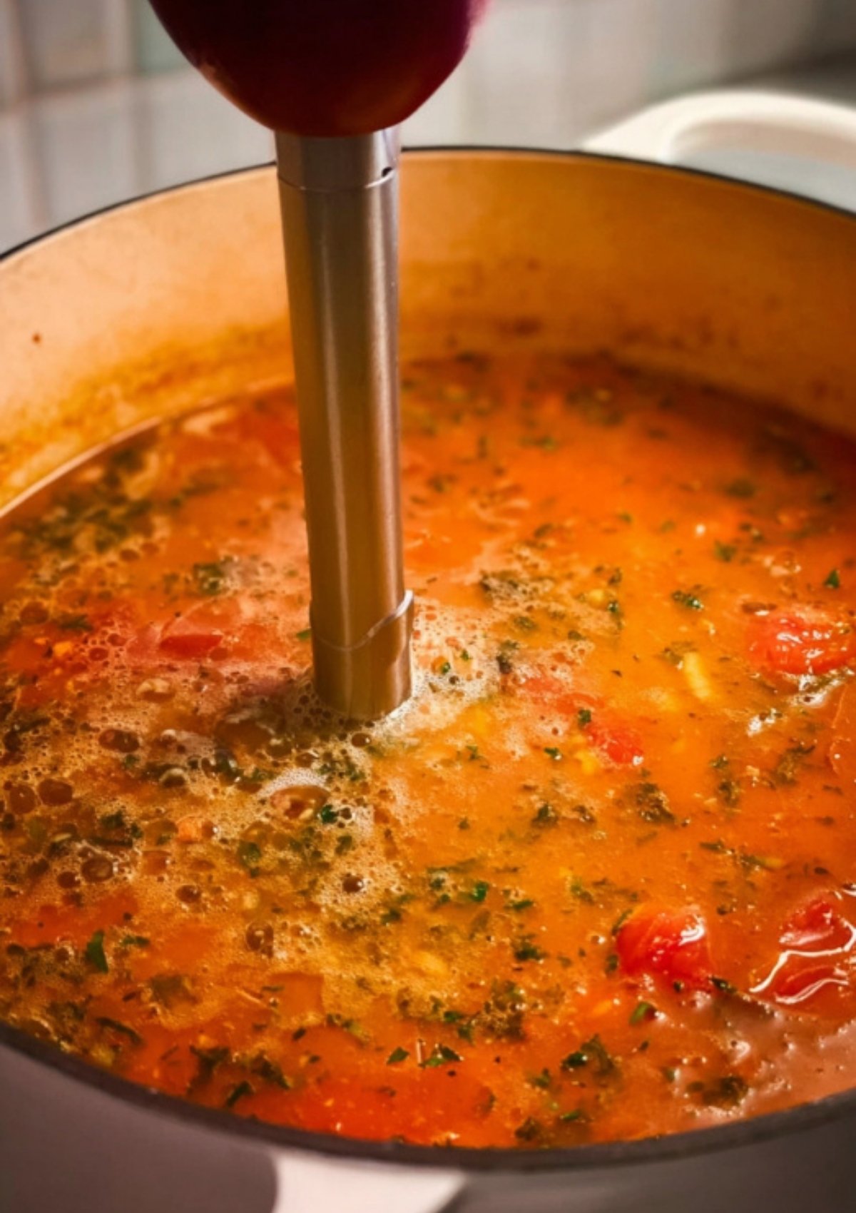 Immersion blender blending tomato soup with herbs in a pot for creamy tomato tortellini soup.