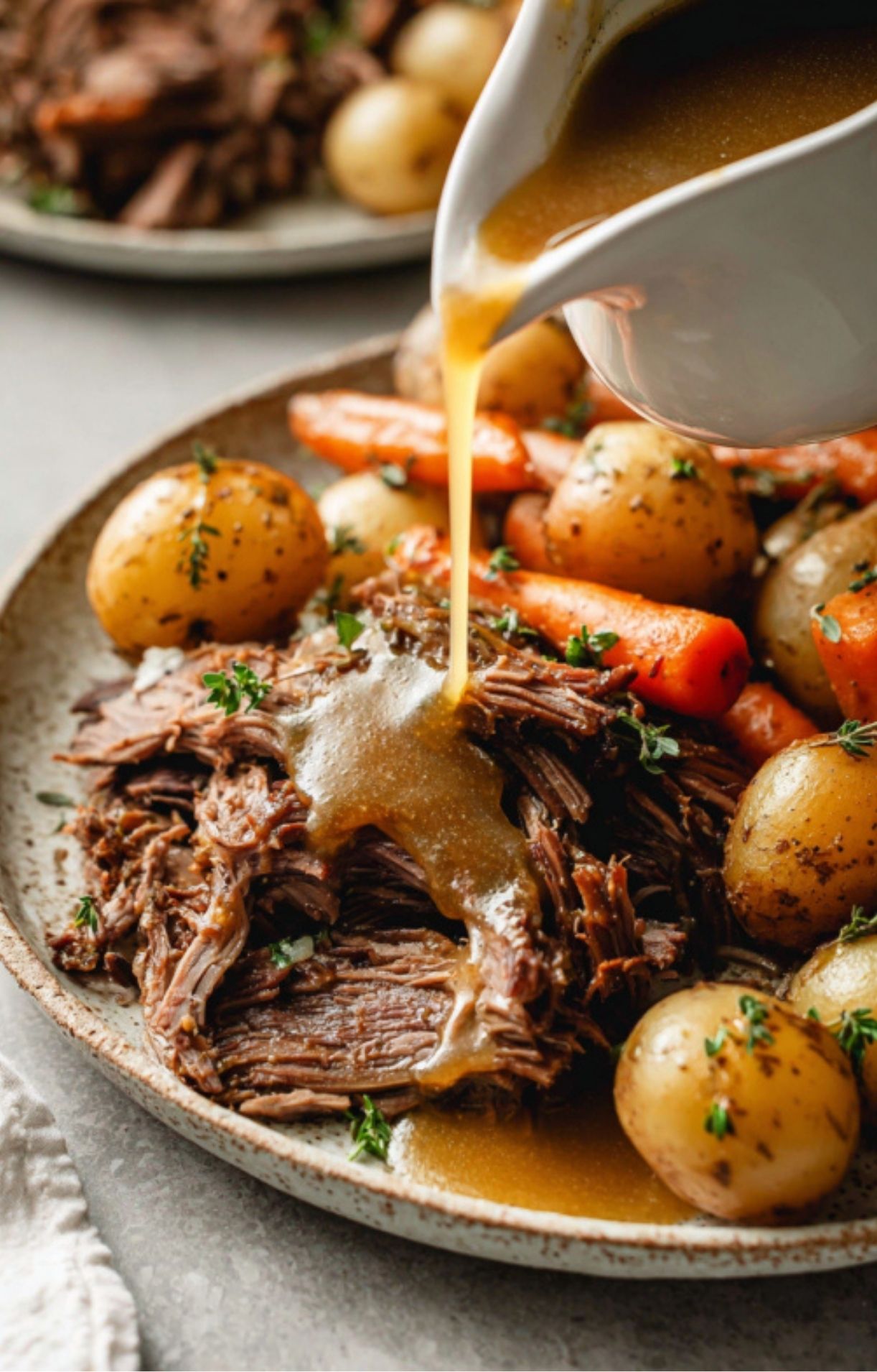Rich brown gravy being poured over shredded crockpot roast beef, potatoes, and carrots for a cozy and satisfying meal.